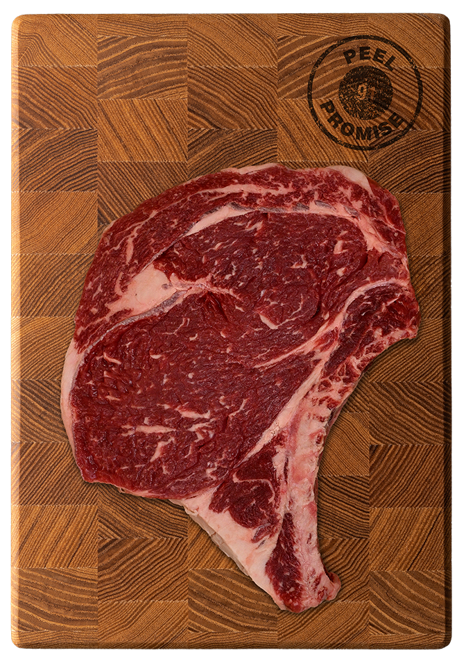 Raw beef steak with marbling on a wooden cutting board that has a circular stamp in the top right corner reading 'PEEL FROMSE'.