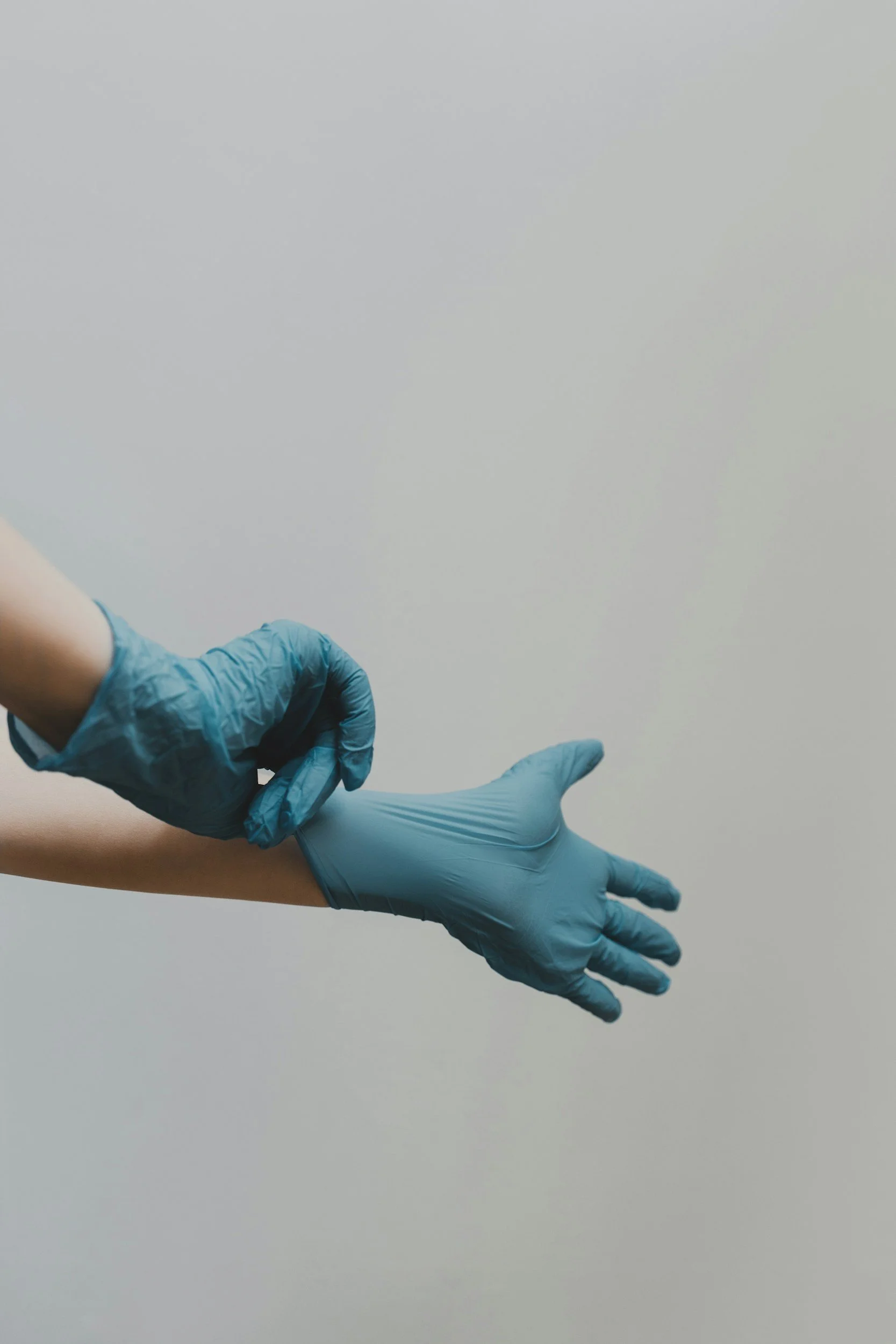 A healthcare worker wearing blue gloves is administering an injection into a person's arm against a plain light background.