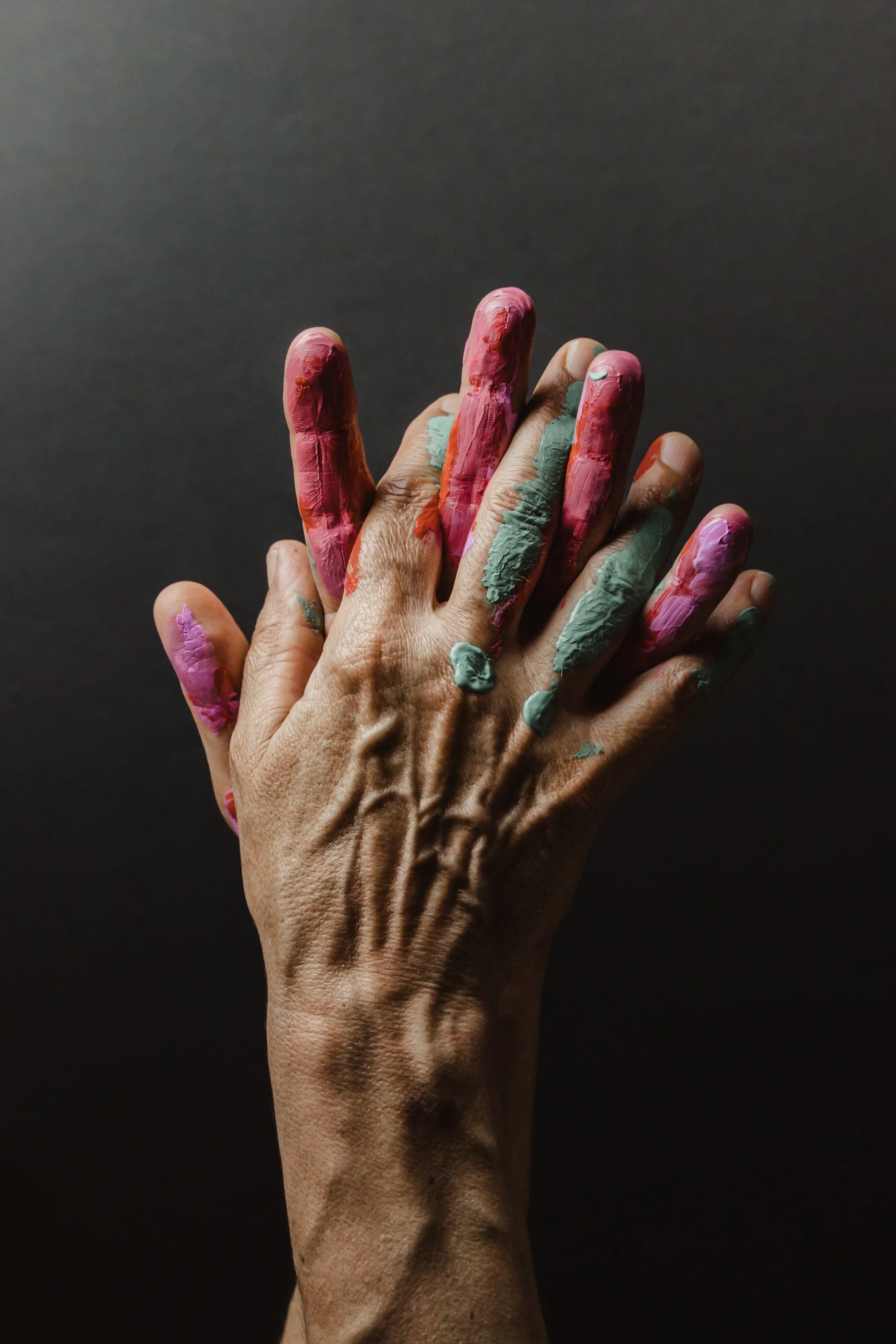 Hand covered in multicolored paint against a dark background.
