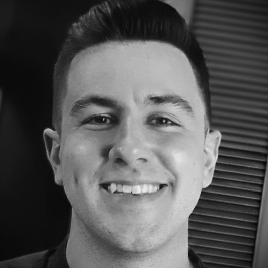 Black and white photo of a smiling young man with neatly styled hair, showing teeth, in front of a background with horizontal lines.