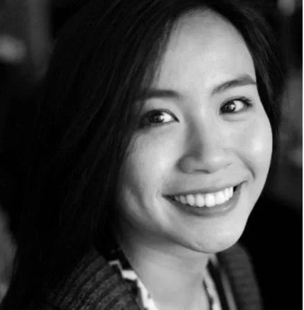 A black and white close-up portrait of a smiling woman with long dark hair.