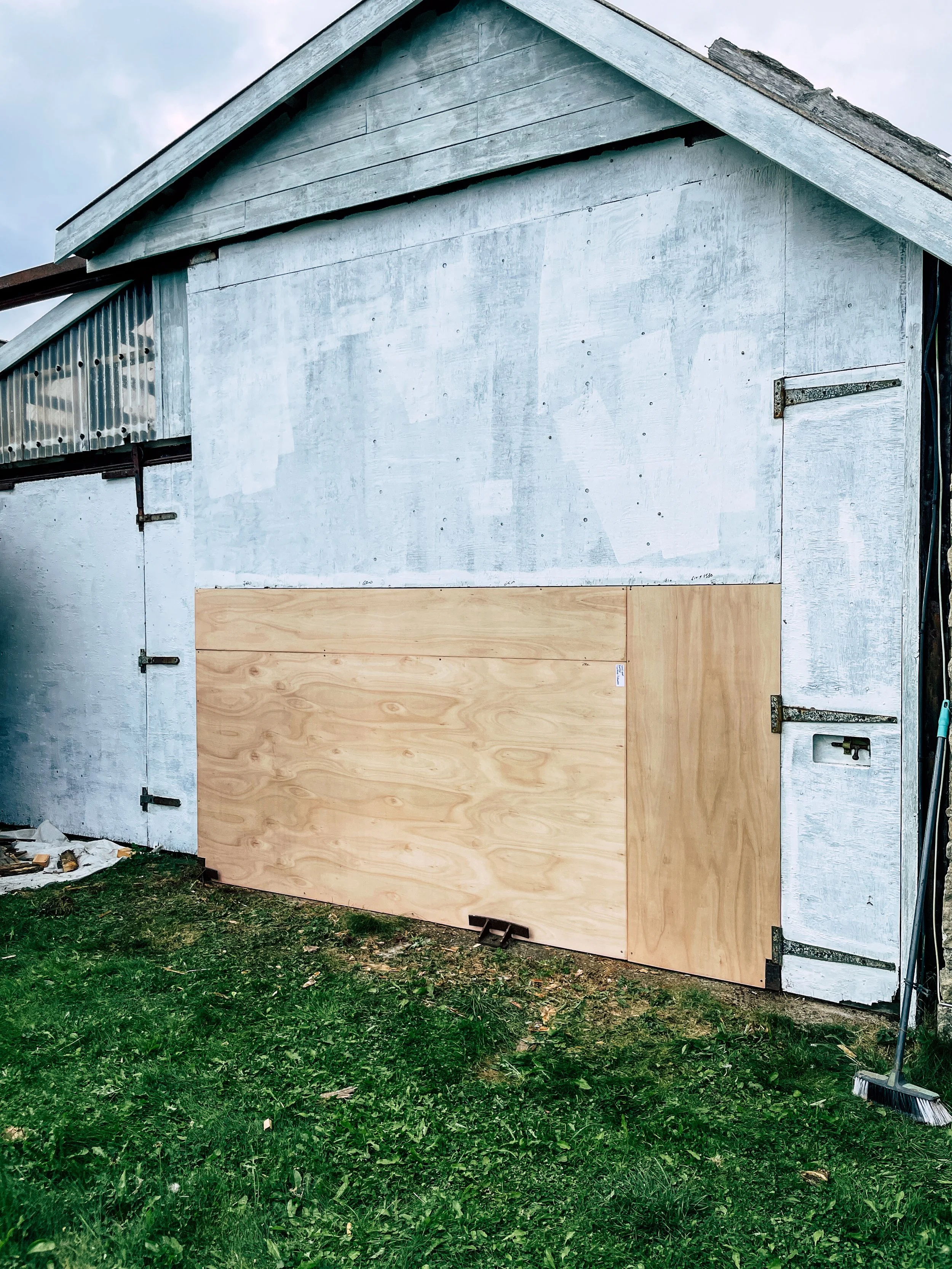 A rustic shed with a boarded-up door, with some hardware and tools visible around it.