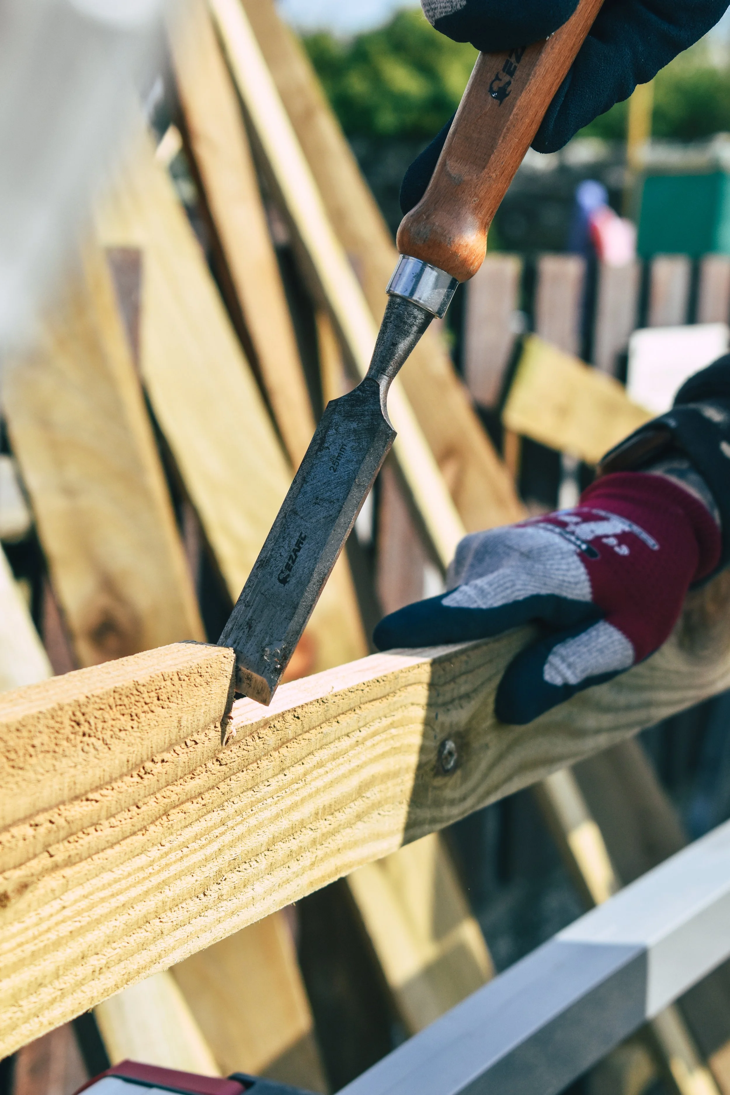 Person wearing gloves using a chisel to carve or cut a piece of wood during woodworking or carpentry project.