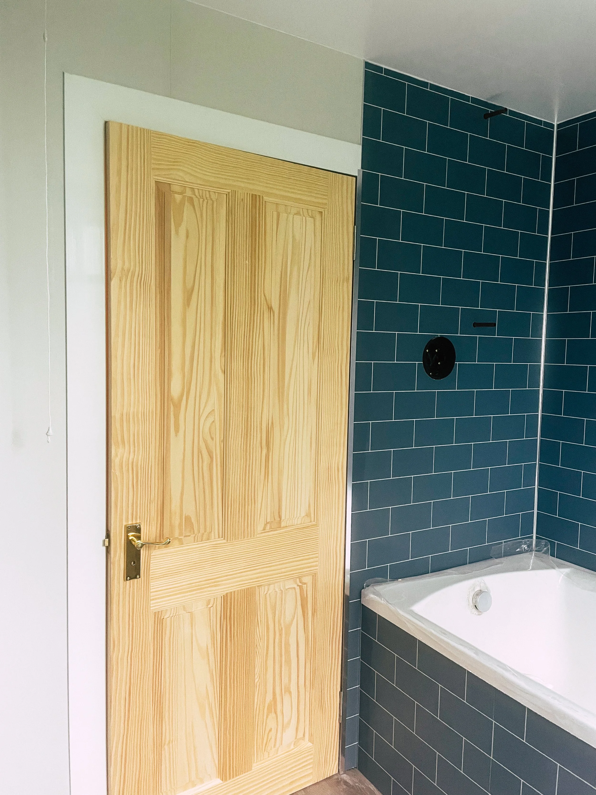A wooden door next to a blue-tiled wall in a bathroom with a bathtub.