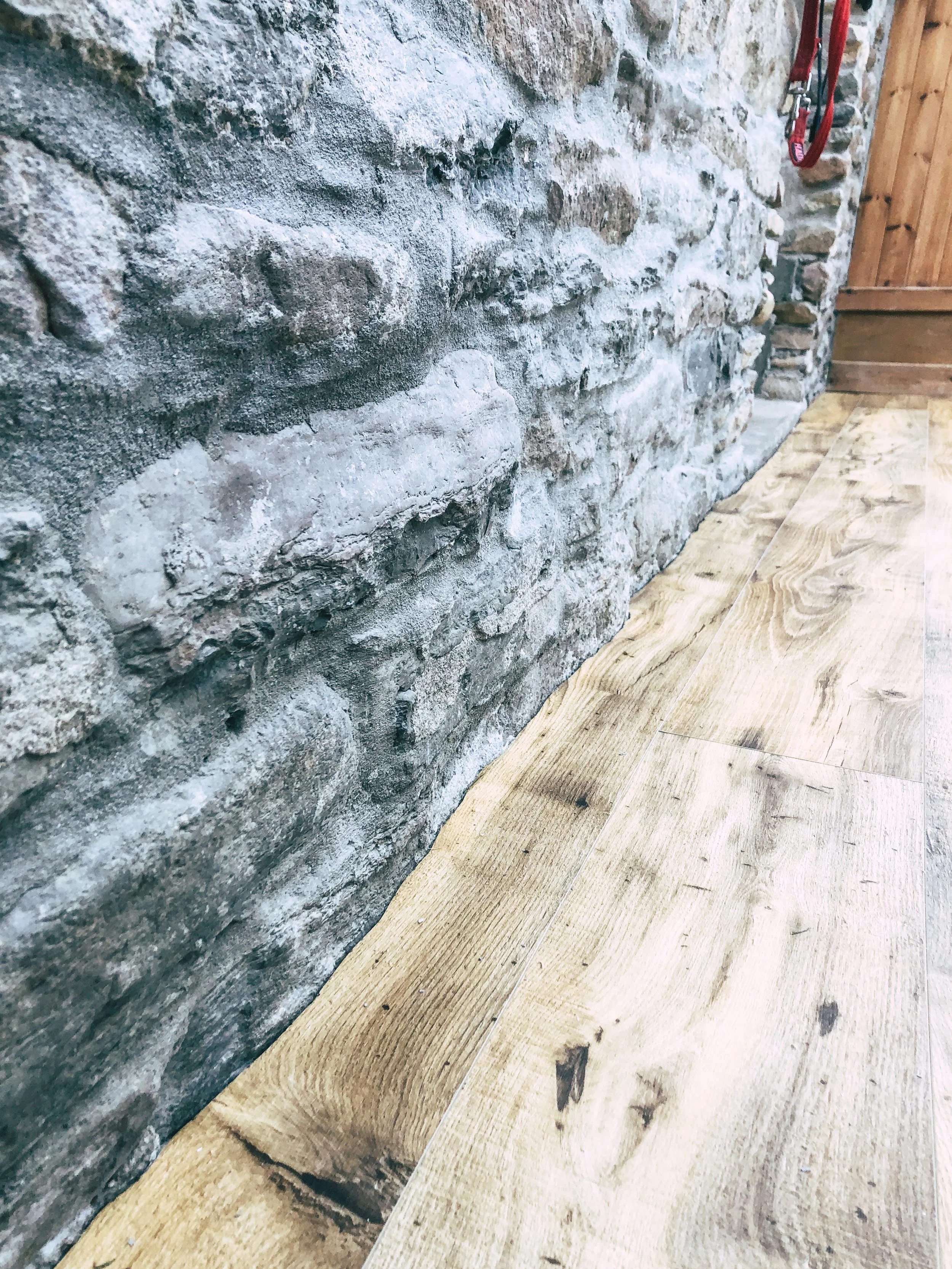 Close-up of a rustic stone brick wall and scribed wooden floor in a room.