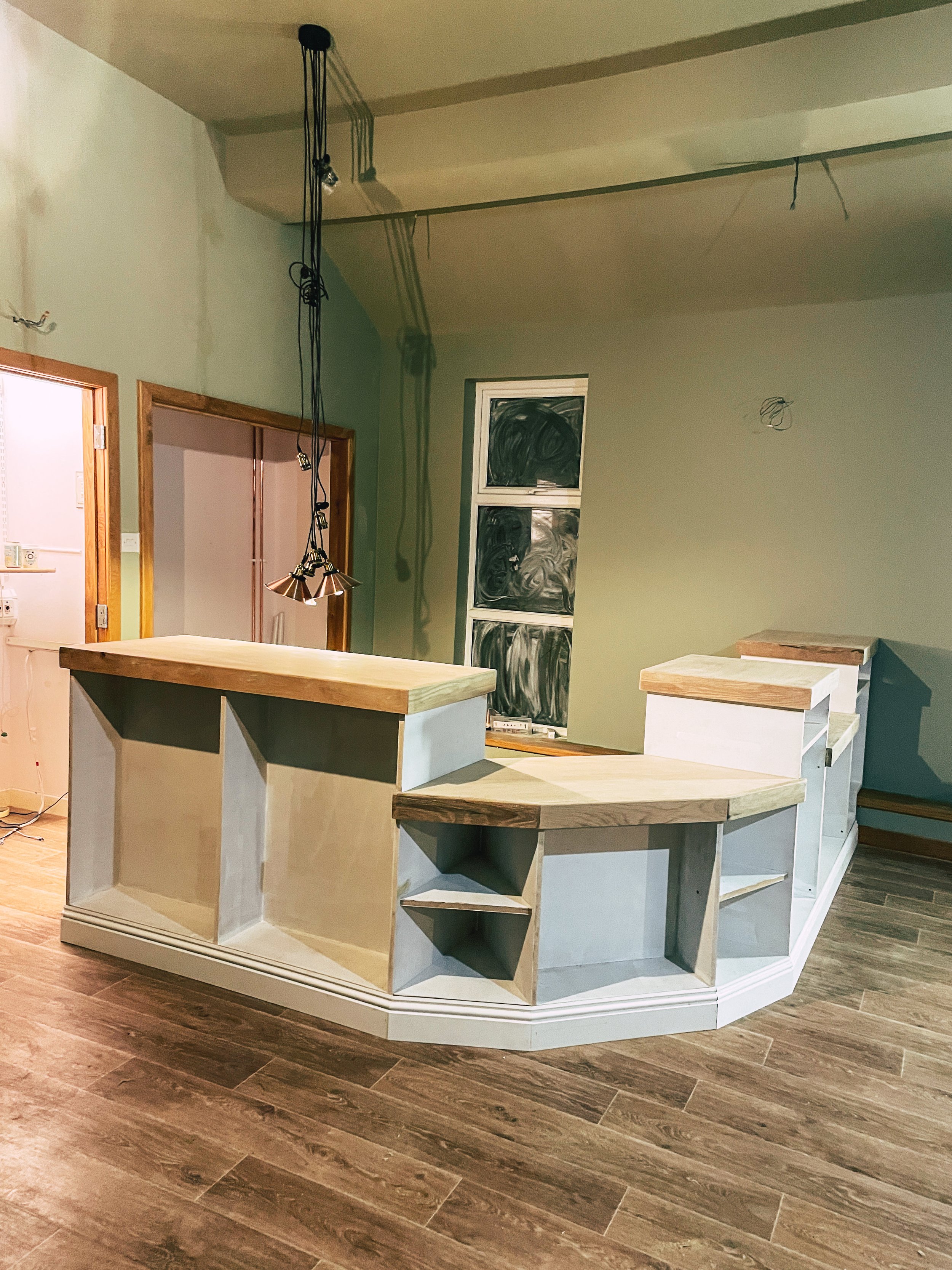 Unfinished kitchen island with wooden countertops and open shelving in a room with wooden flooring and incomplete ceiling.