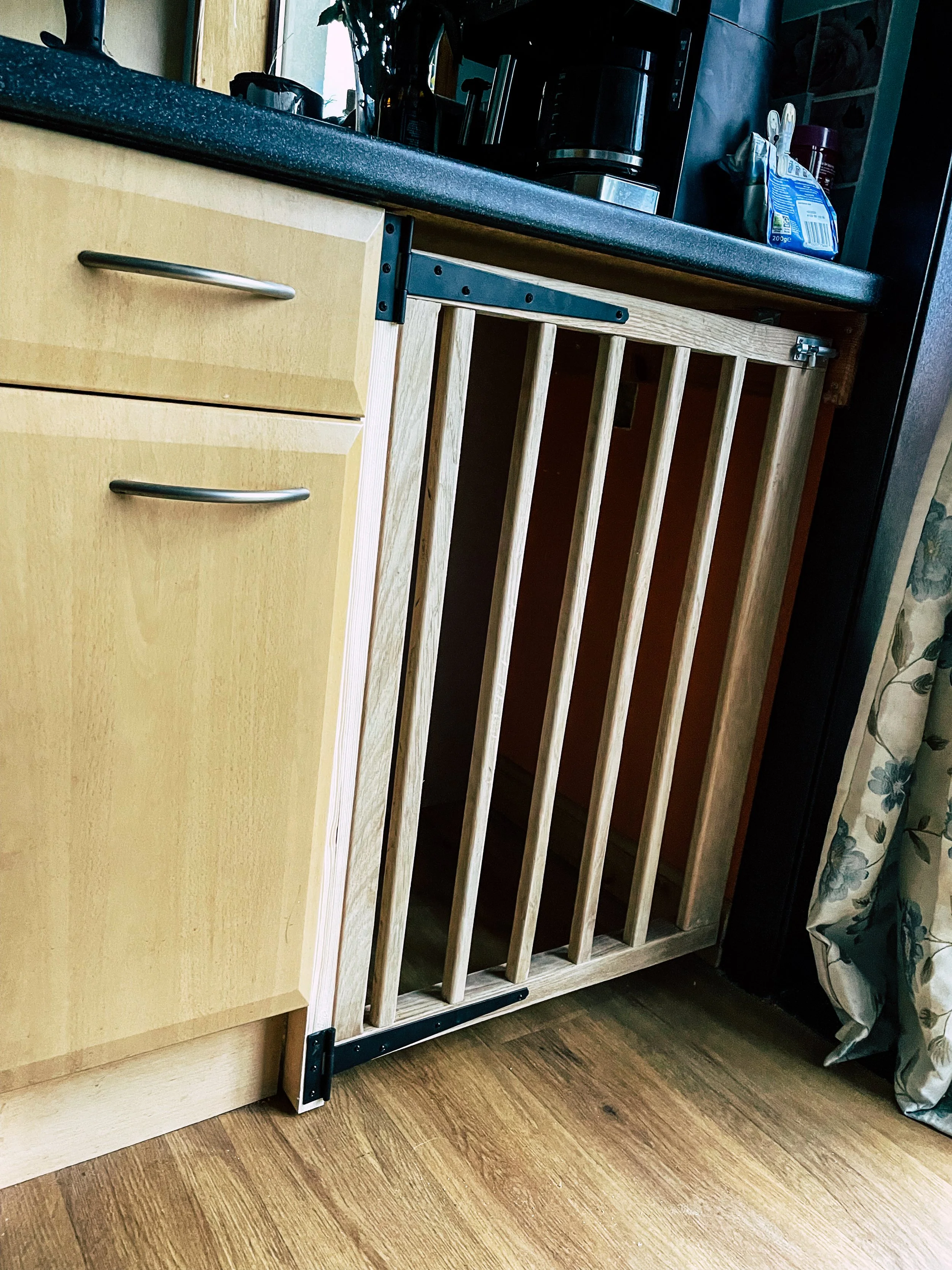 A wooden dog gate installed in a kitchen doorway with a black countertop and cabinets.