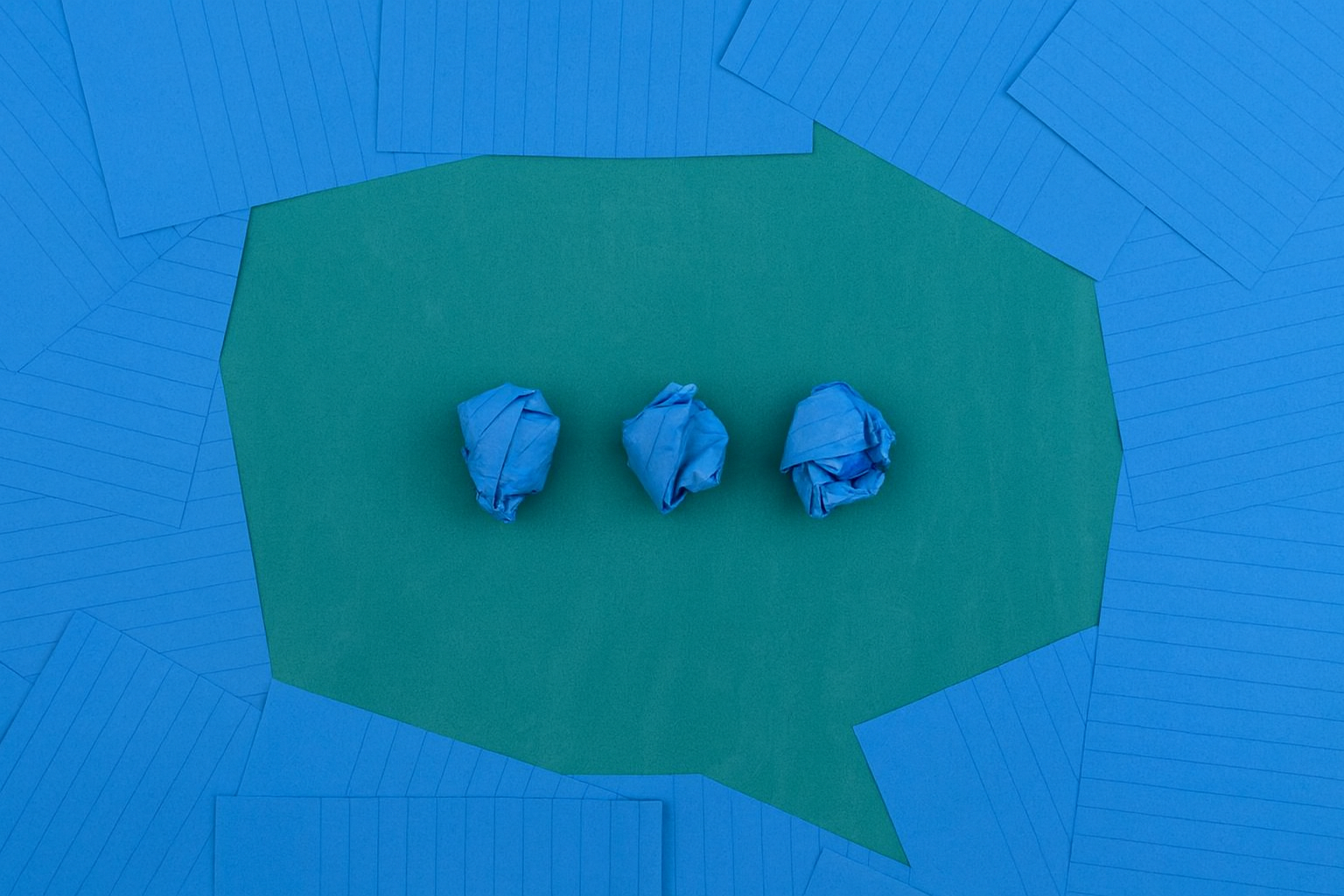 Three crumpled blue paper balls on a green speech bubble-shaped paper with a blue background of scattered blue sheets.