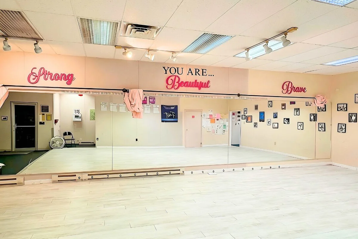Empty dance studio with a large mirror, motivational words on the wall, and wall decor including framed pictures.