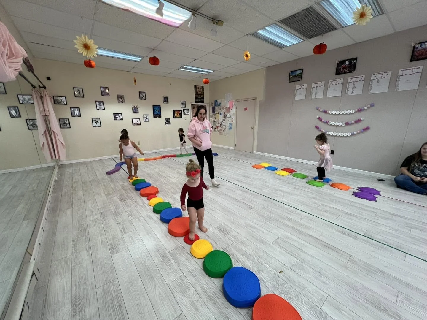 Children participating in an indoor activity, walking on colored stepping stones arranged in a line across a dance studio with decorated walls and ceiling.