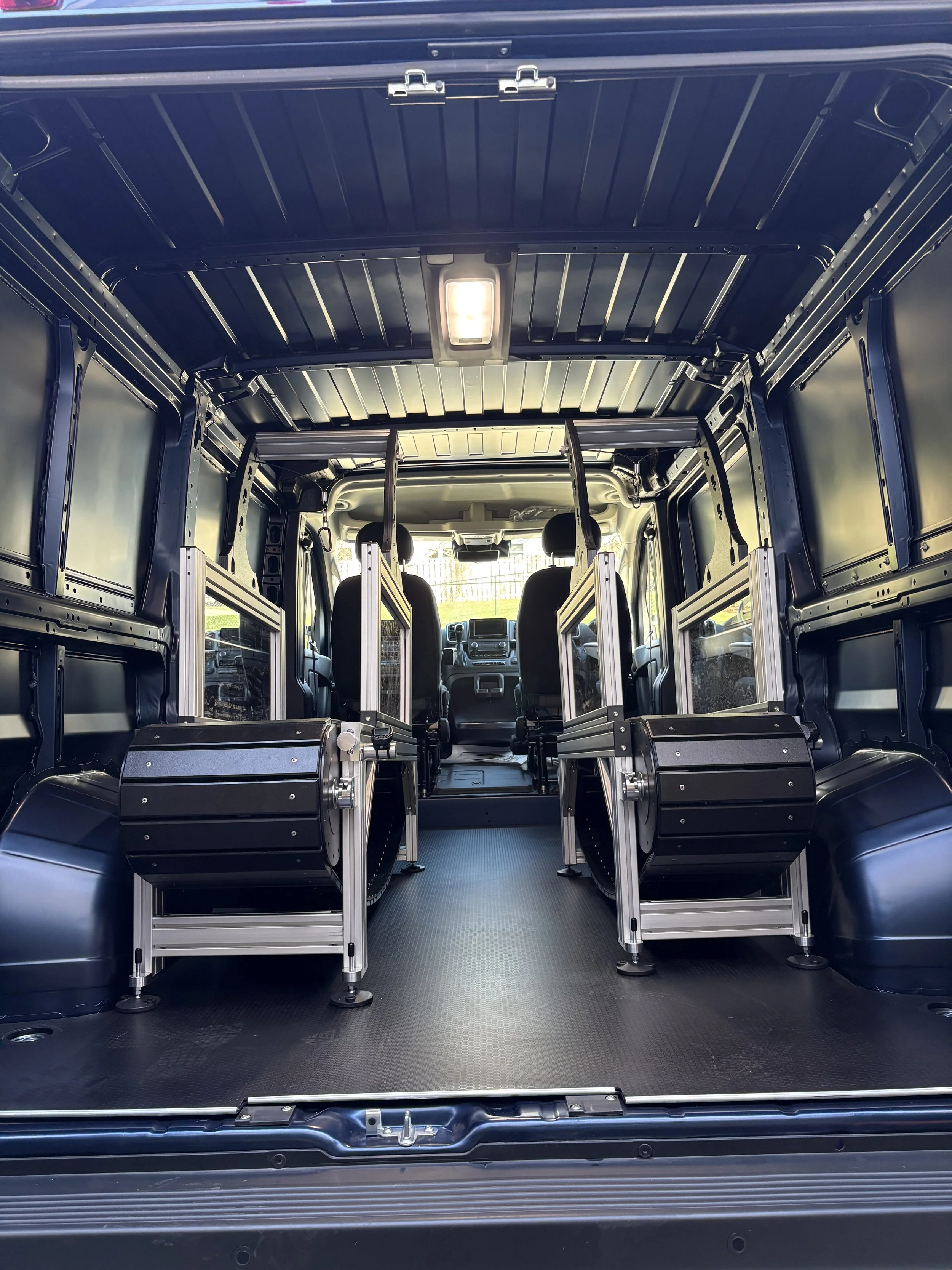 Interior view of a van with metal shelving and a bench, front seats, and a ceiling light.