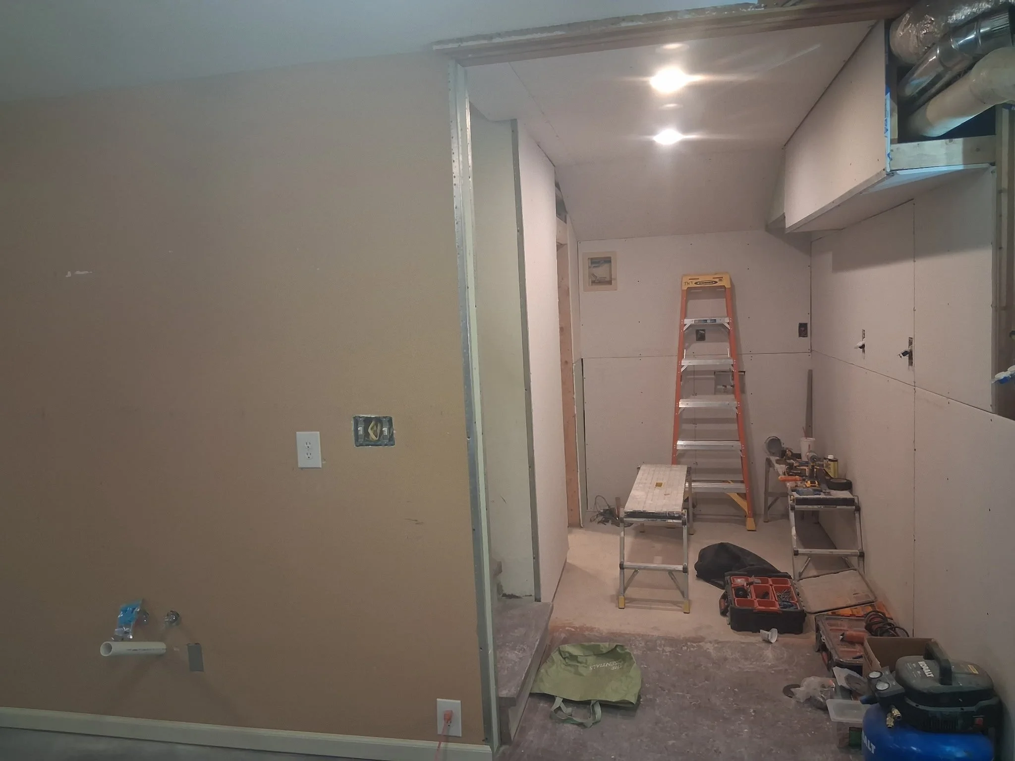 Interior room under renovation with drywall installation, a ladder, tools, and construction materials scattered on the floor.