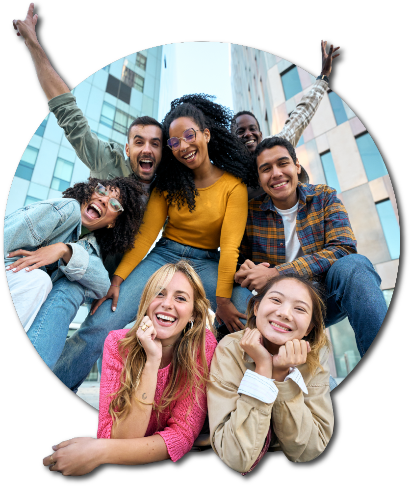 Group of happy hotel guests - diverse young adults smiling and posing together outdoors in an urban setting with hotel building in the background.