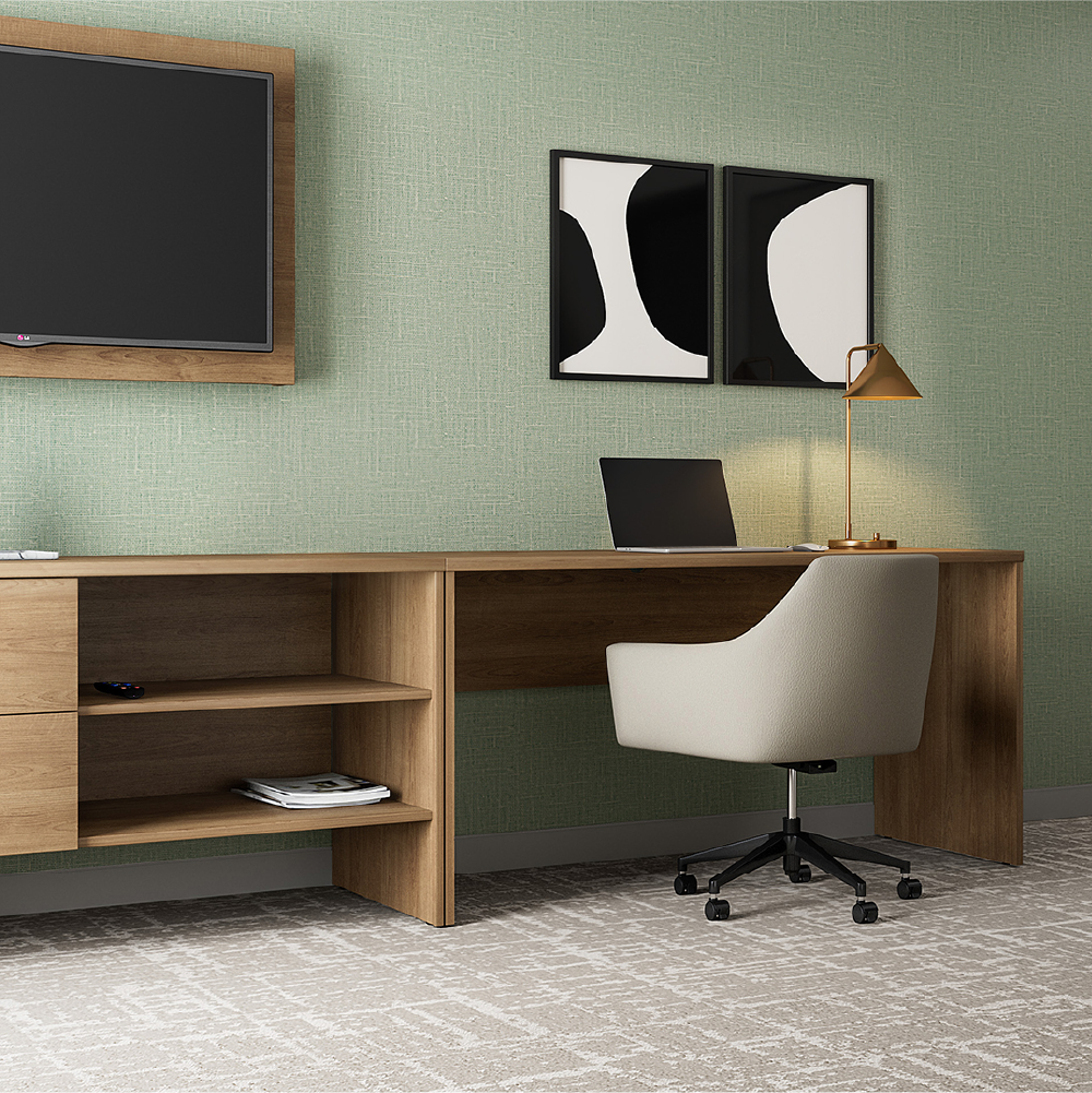 A prototypical hotel room for Best Western, with a wooden desk, white office chair, and a computer laptop. On the desk, there is a gold desk lamp. The wall behind has green textured wallpaper with two black and white abstract art pieces.