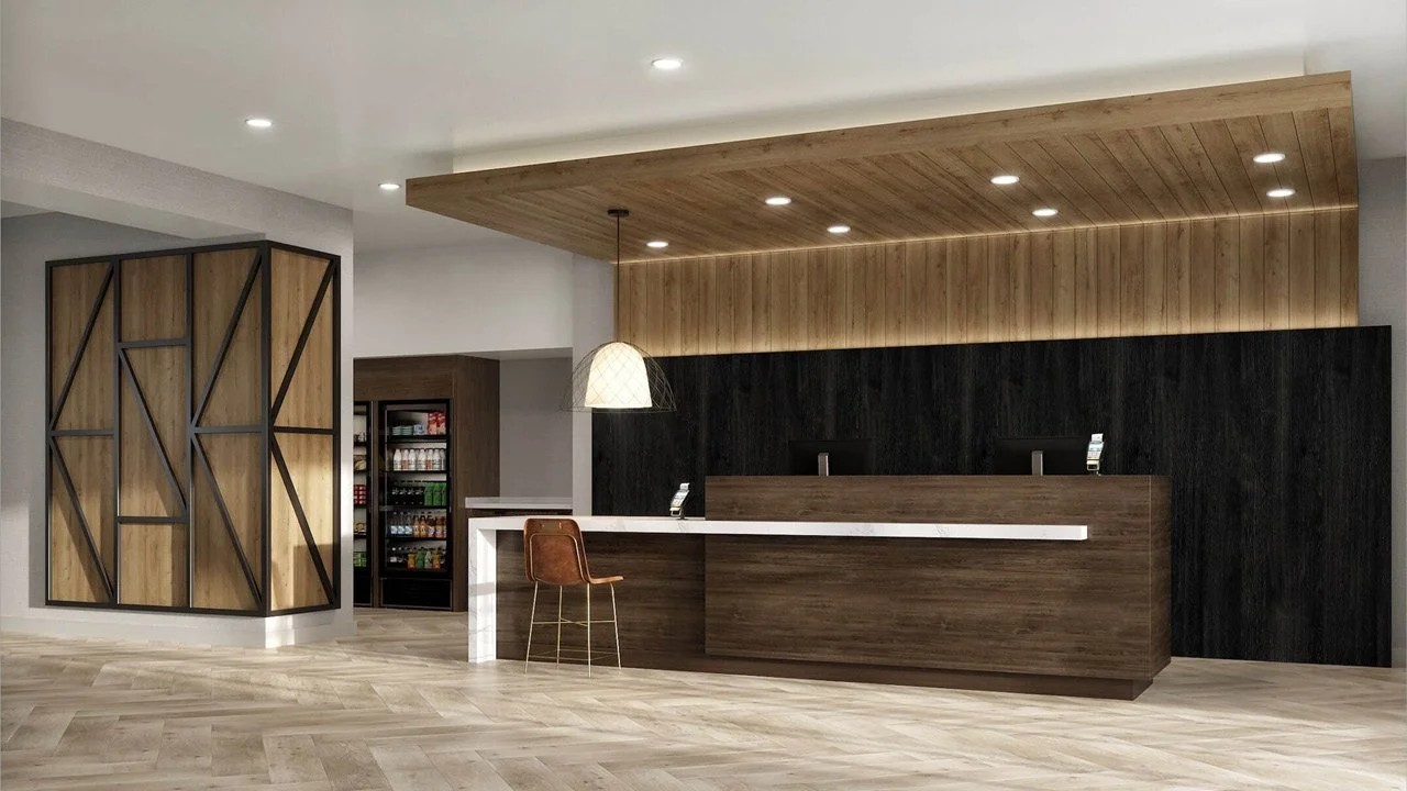Modern prototypical Staybridge hotel by IHG reception area and front desk with wooden accents, a counter with two monitors, a single brown chair, and a beverage vending machine in the background.