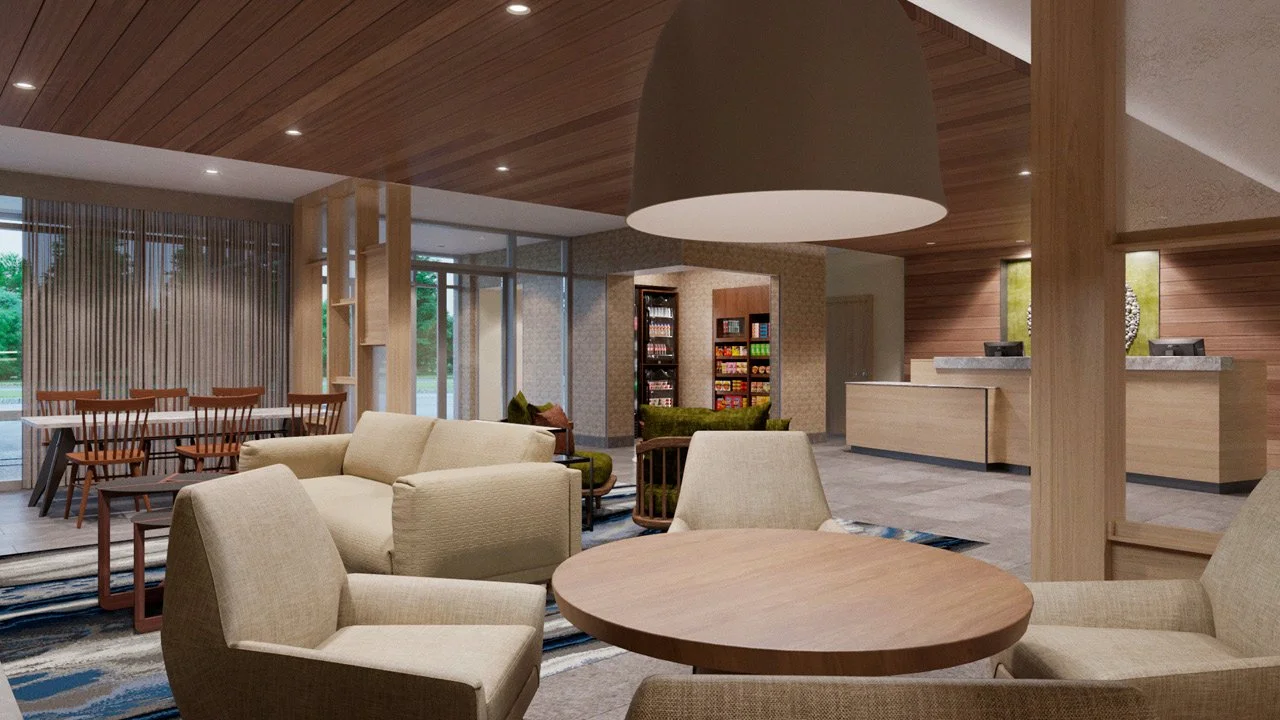 Modern prototypical public area by Fairfield Inn and Suites by Marriott,  with beige sofas, wooden chairs, a table, a reception desk, and a vending area with snacks; large windows showing greenery outside.