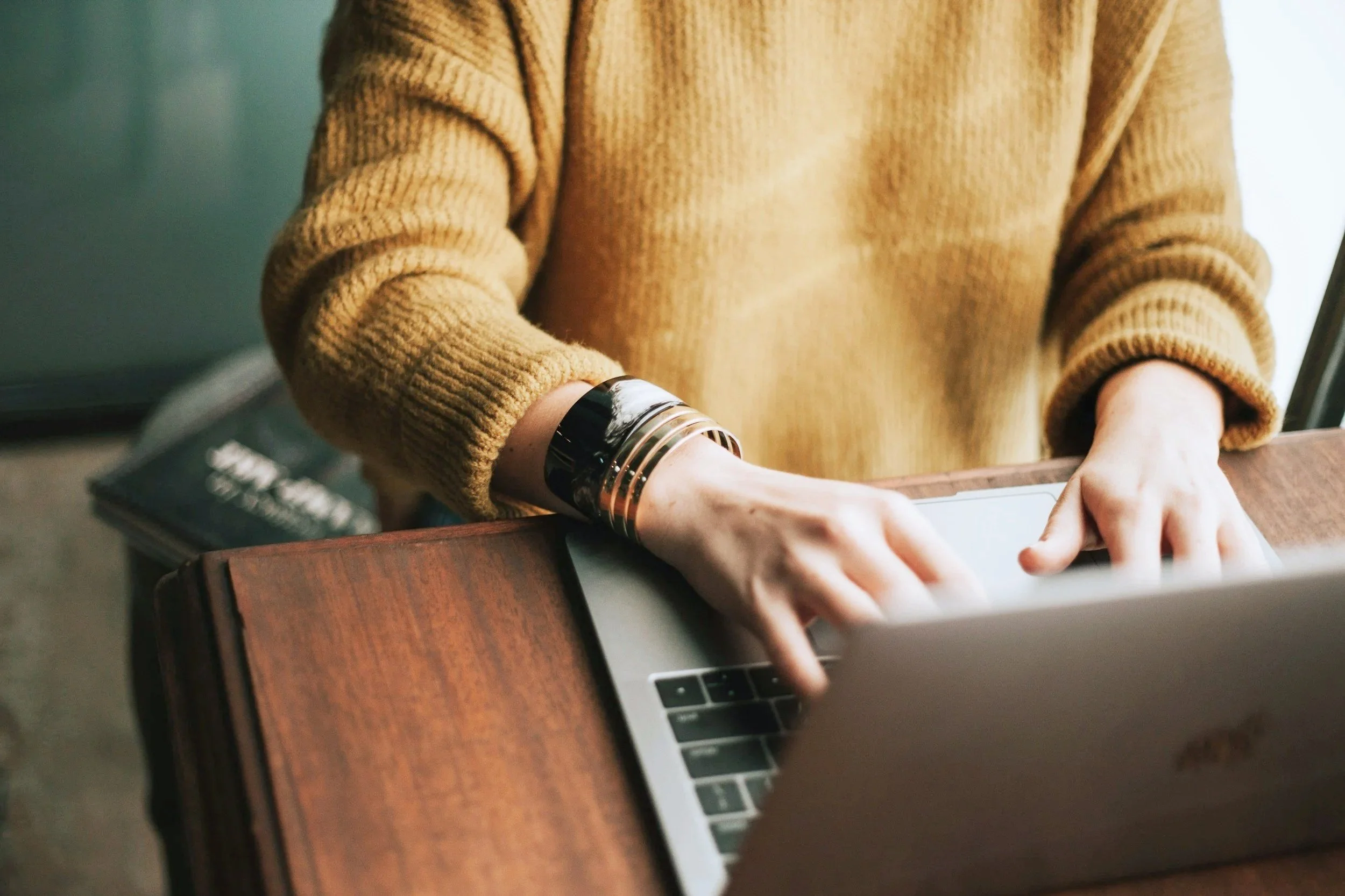 Person wearing a mustard sweater using a laptop at a wooden table.
