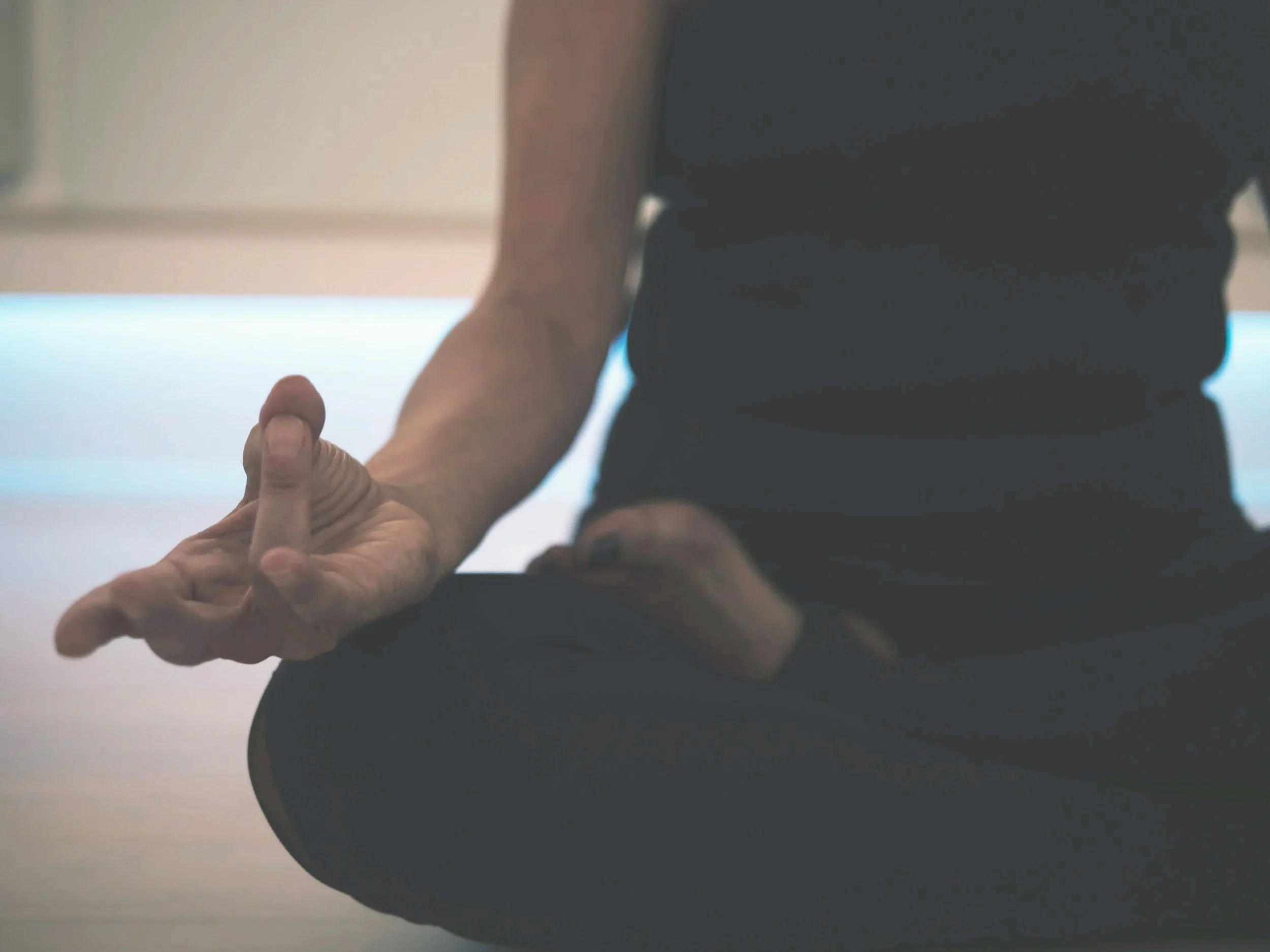 Person sitting cross-legged practicing yoga or meditation, with left hand resting on knee and thumb and index finger touching.