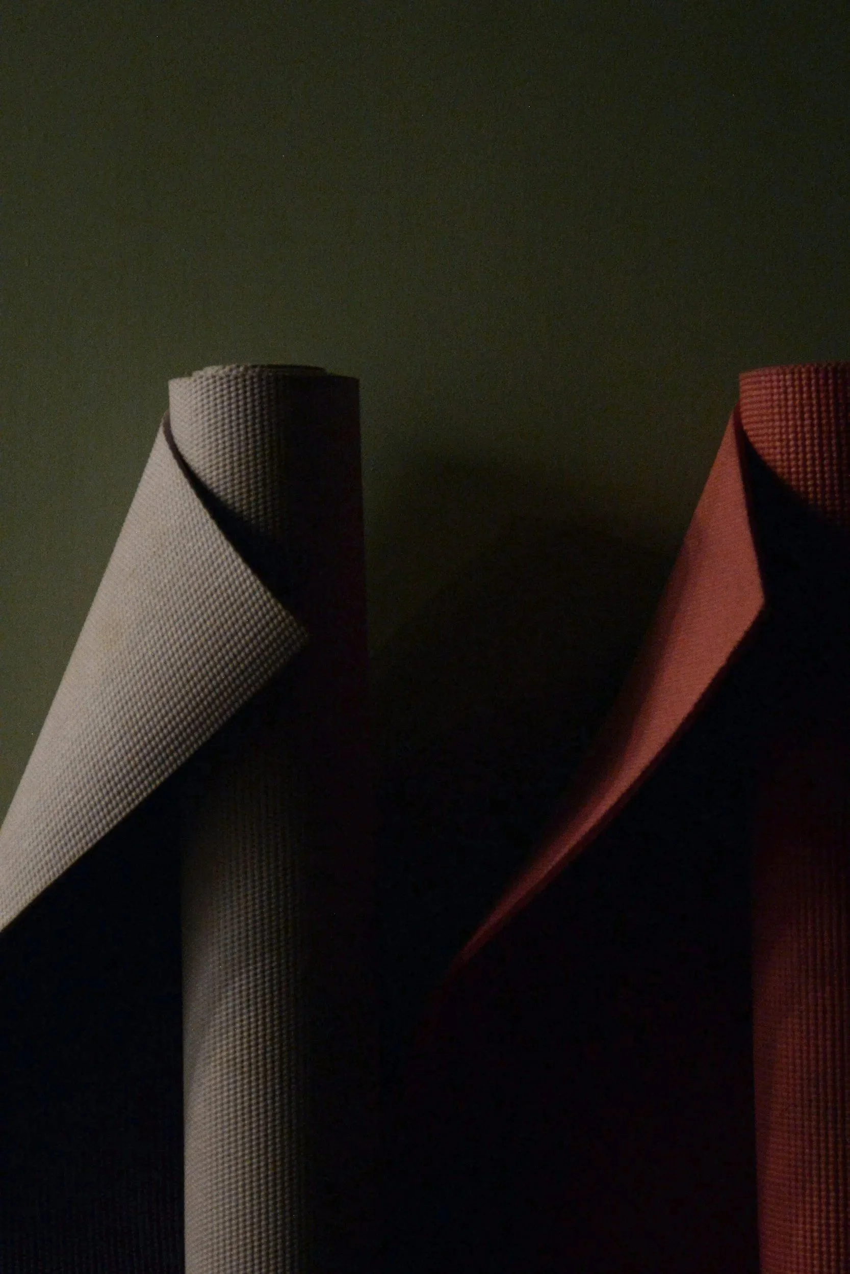 Close-up of two rolled-up mats or fabrics, one beige and one reddish-brown, standing vertically against a dark background.