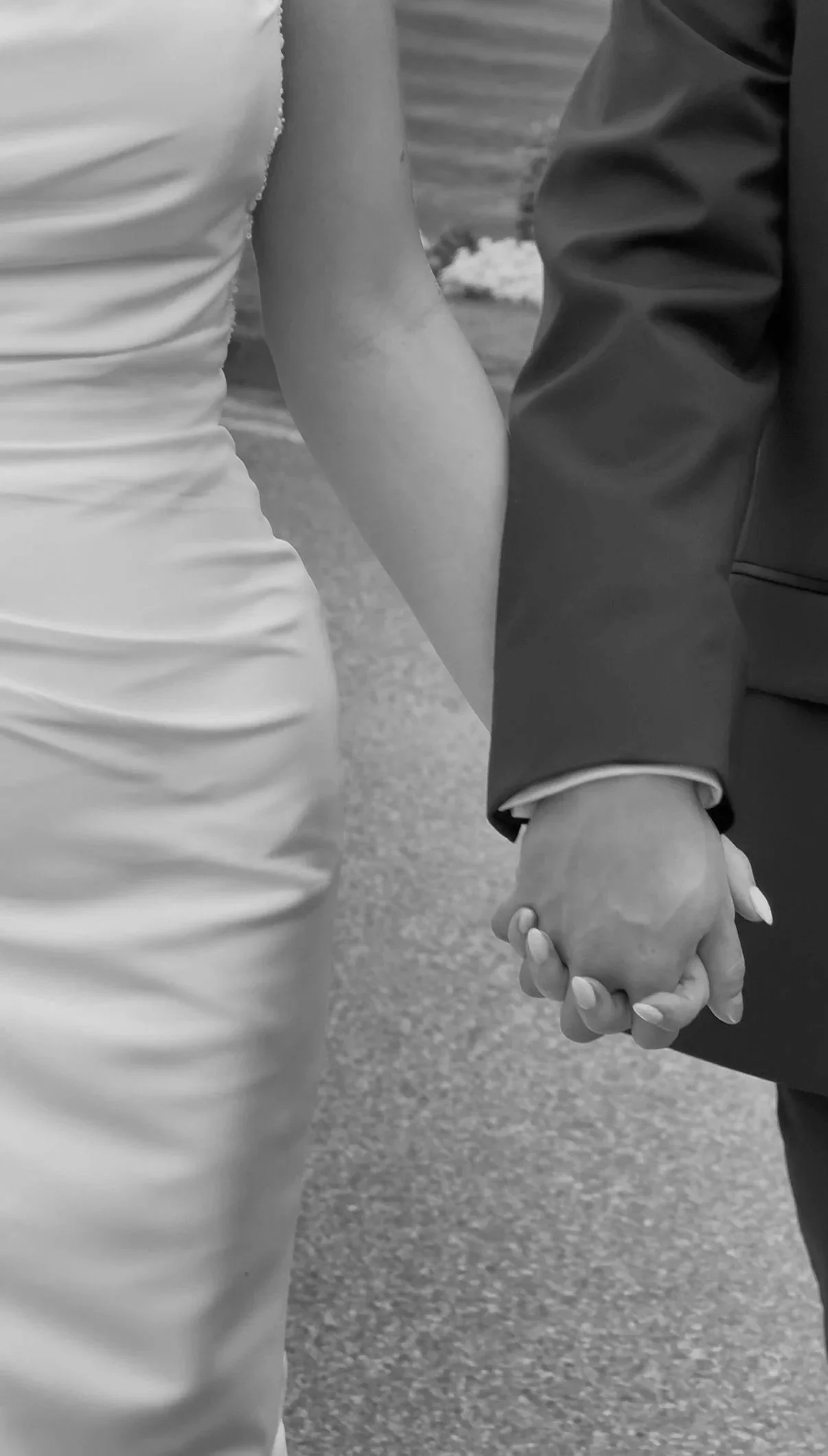 A close-up black-and-white photo of a couple holding hands, with the woman wearing a fitted dress and the man in a suit.