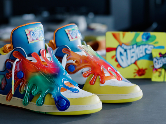 Colorful sneakers with rainbow splash paint design, placed on a surface with a box of slime toys in the background.