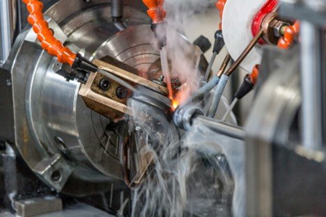 A metalworking lathe machine performing a welding or grinding process with sparks and smoke.