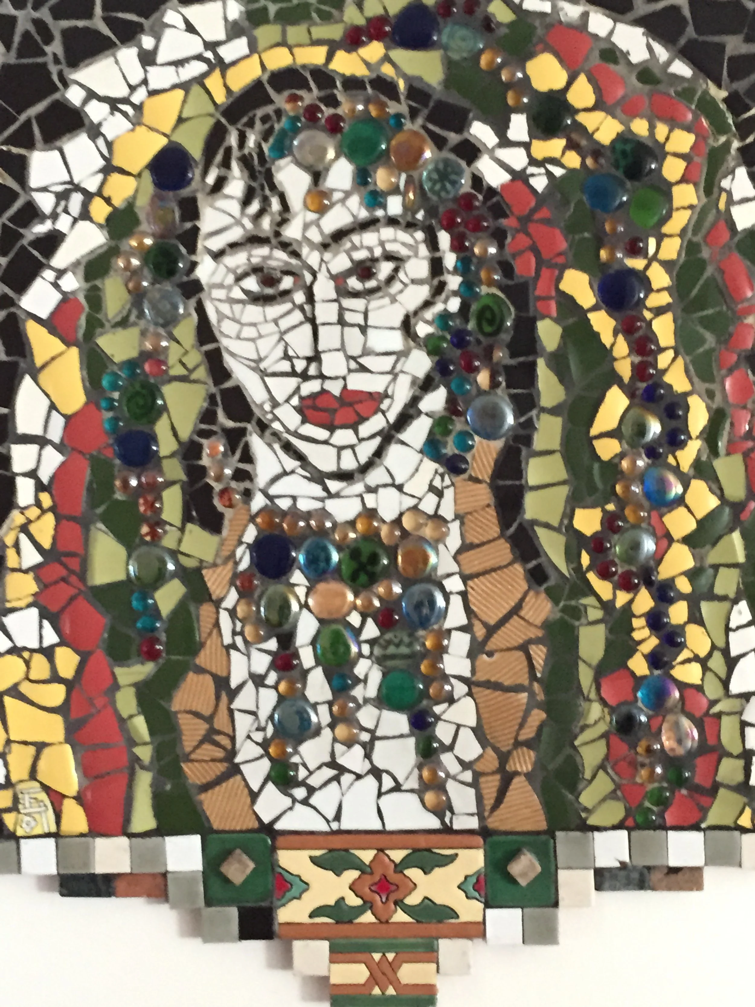Mosaic artwork featuring a portrait of a woman with curly hair, wearing a necklace, surrounded by colorful geometric and floral patterns.
