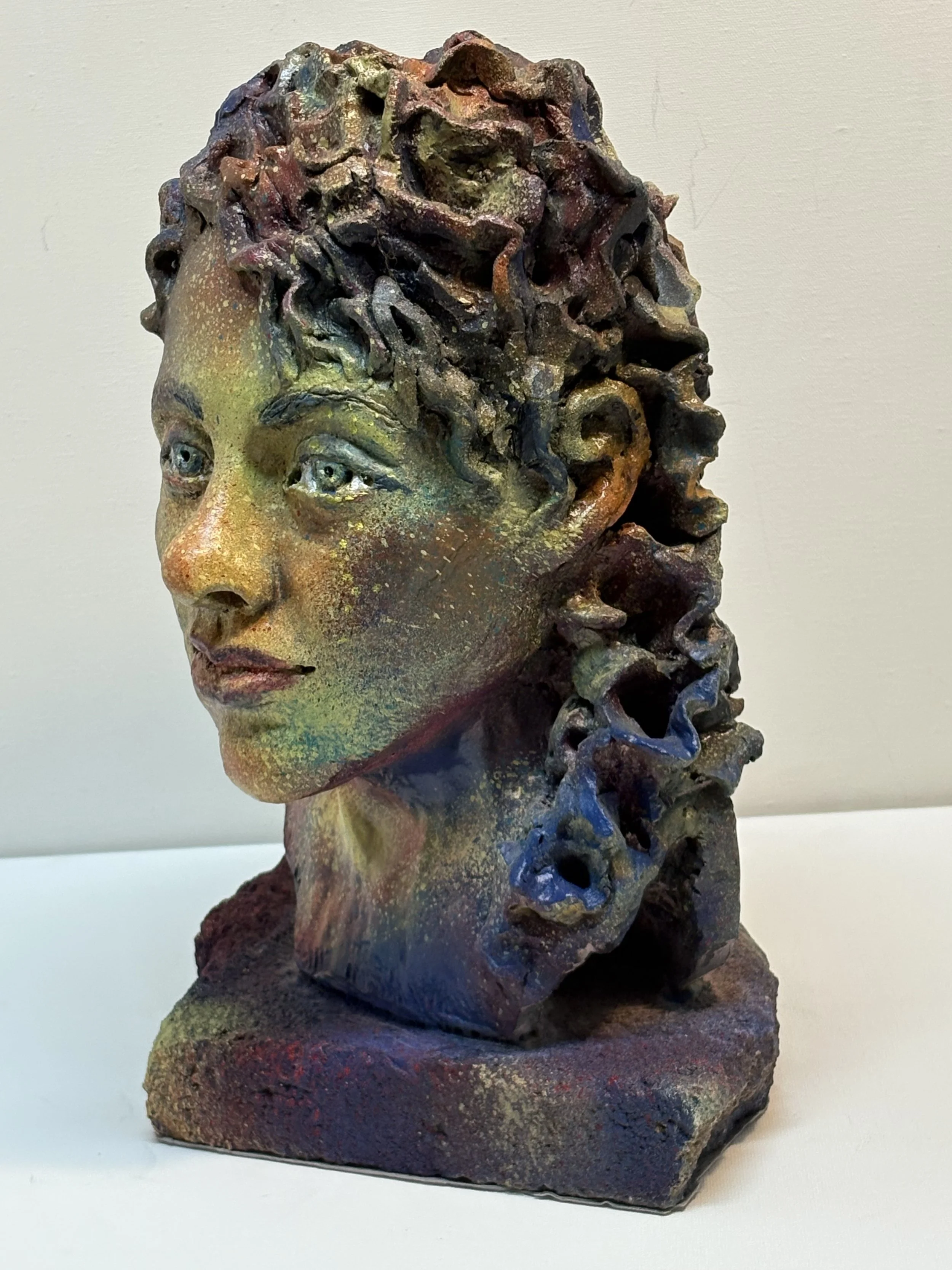 Colorful sculpture of a woman's head with curly hair and detailed facial features, placed on a textured base.