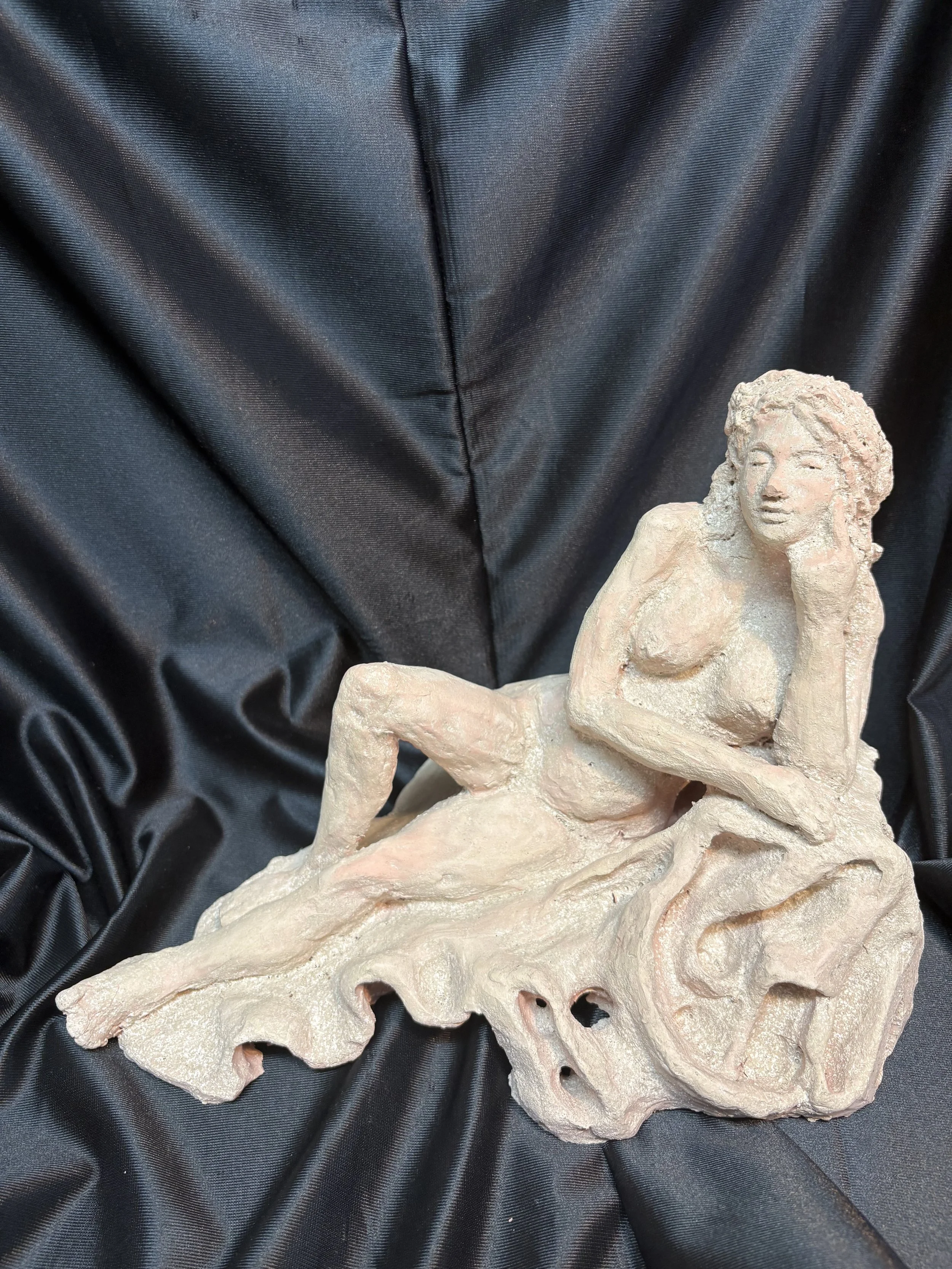 A nude ceramic sculpture of a woman lying on a flowing, abstract base, placed on black fabric.