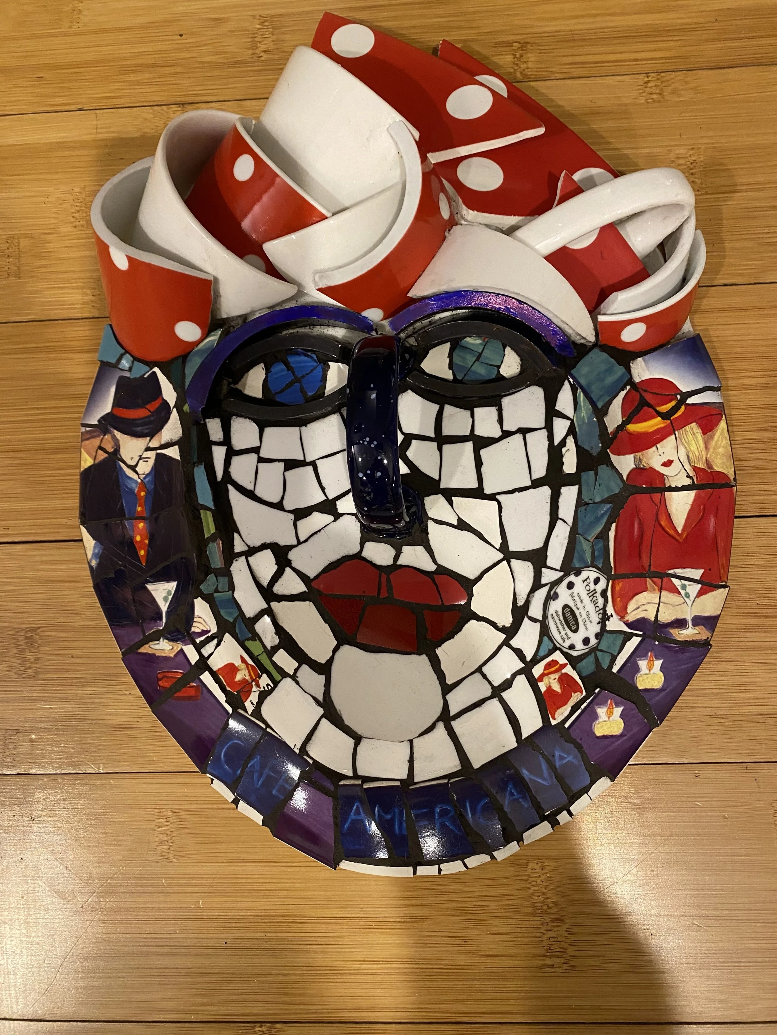 A Mosaic head-shaped sculpture made from broken ceramic cups and plates with a face design, displayed on a wooden floor.