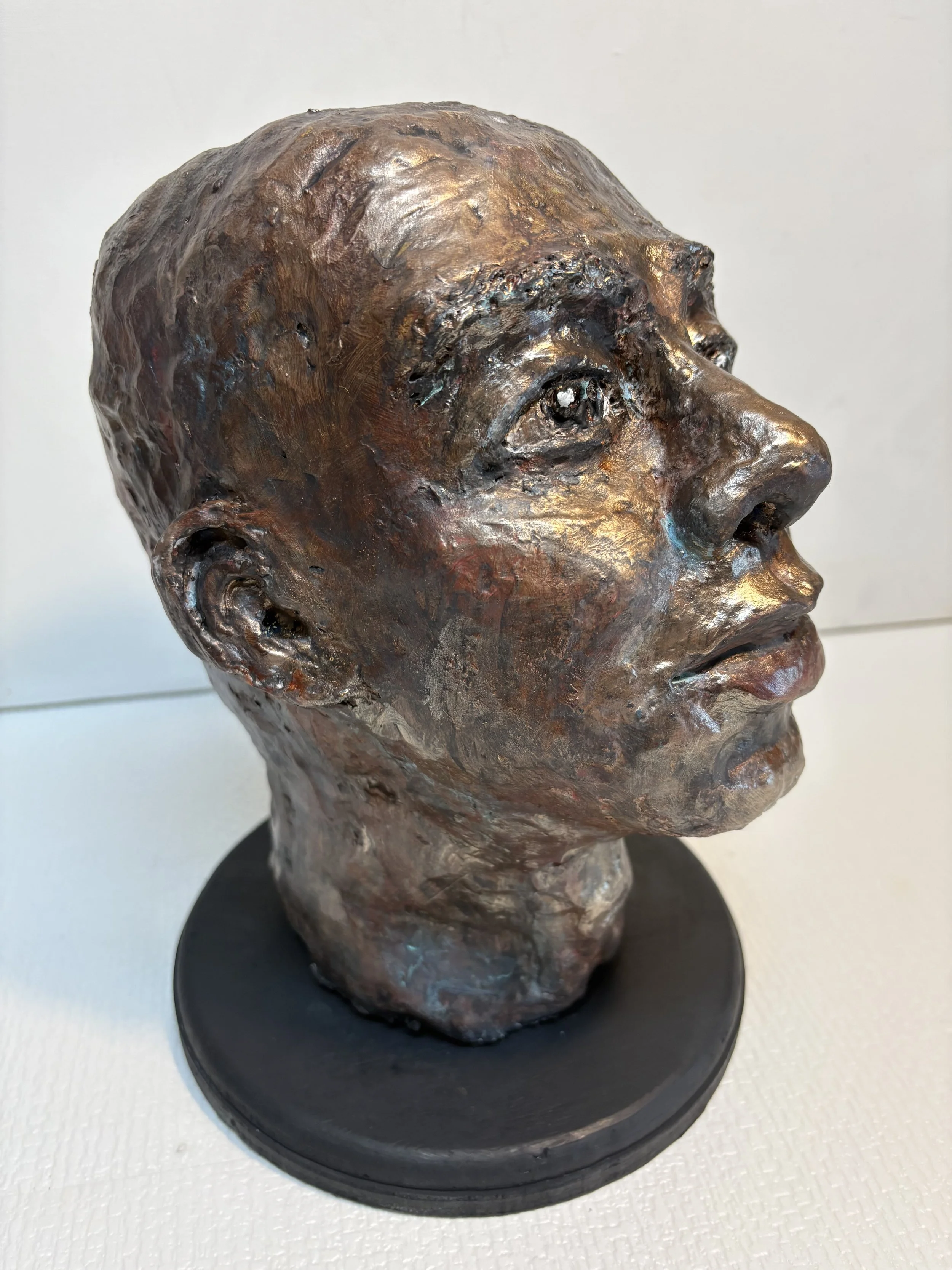 Bronze sculpture of a person's head in profile, displayed on a black circular base.