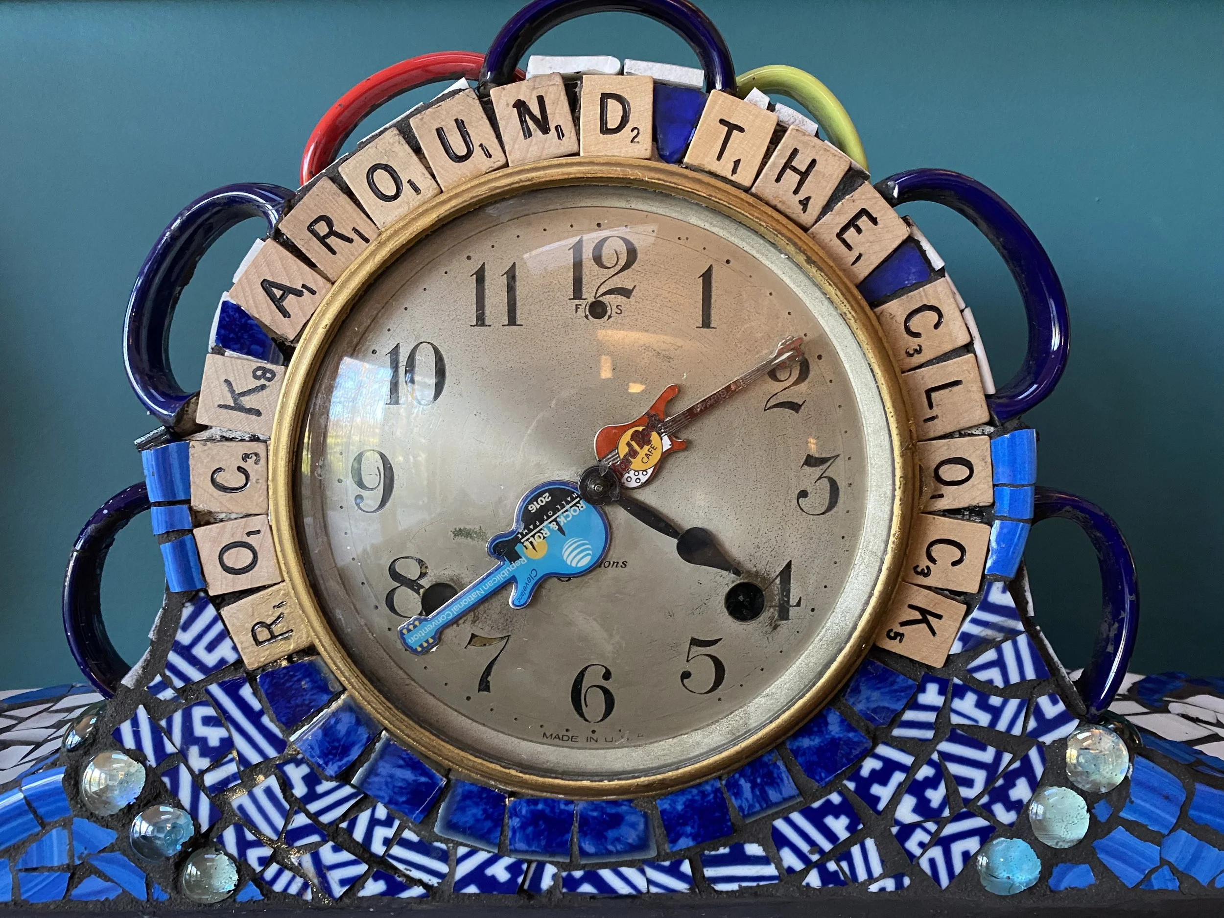 Decorative clock made with mosaic tiles, with wooden alphabet tiles around the face spelling 'AROUND THE CLOCK'.