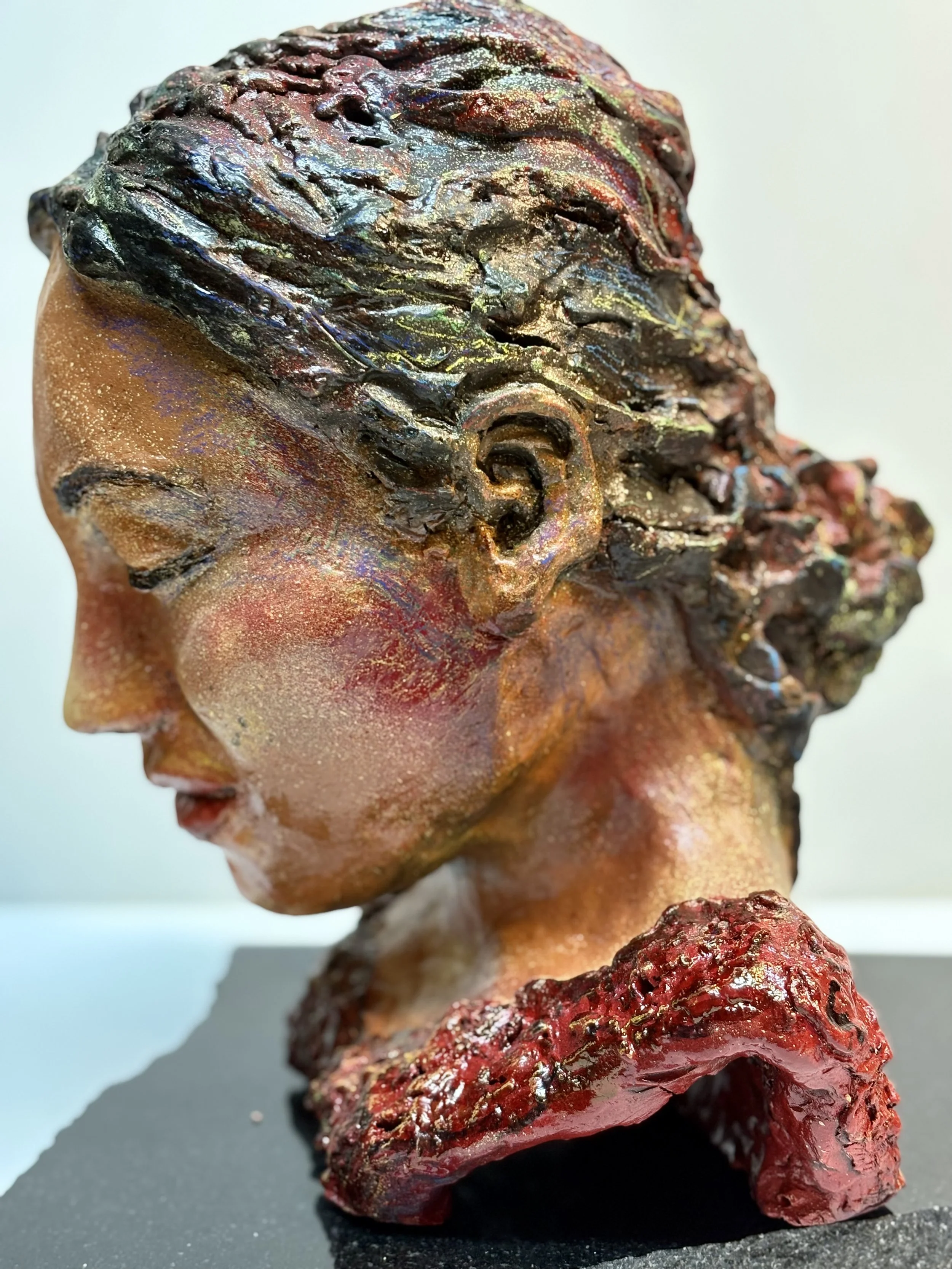 A colorful sculpture of a woman's head in profile, with textured, multicolored hair and an abstract, red sculpture at the base.