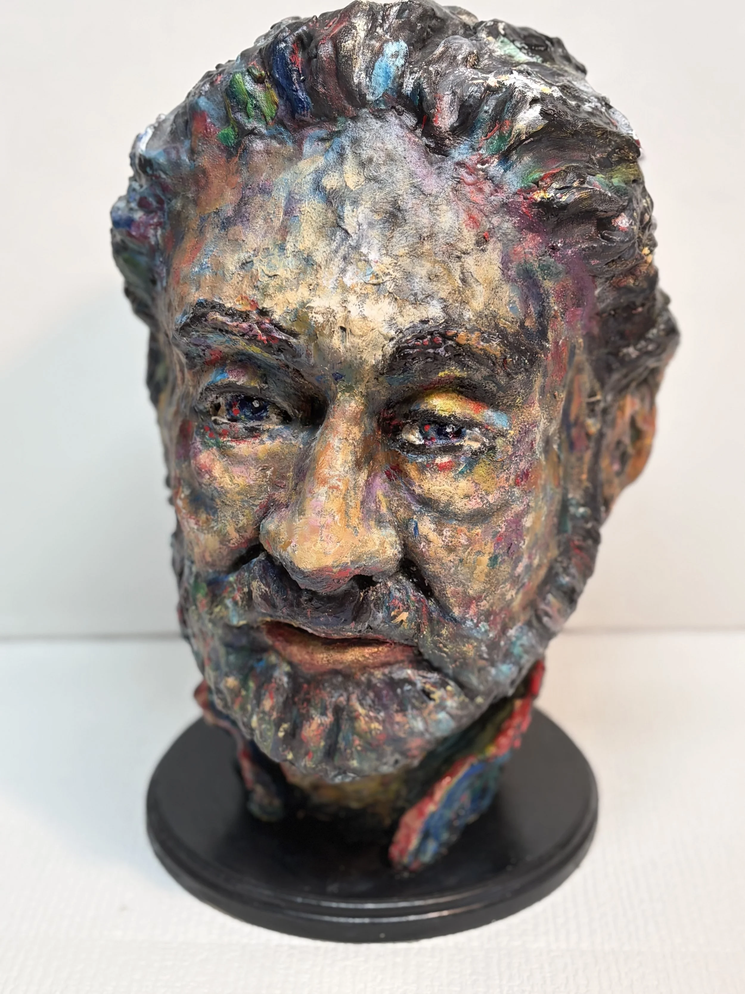 Colorful, textured sculpture of a man's face with a beard, mounted on a black stand.