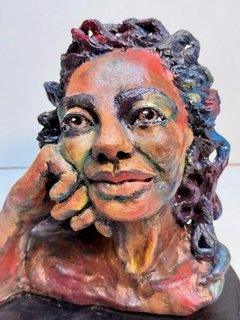 Colorful sculpture of a woman with one hand resting on her chin, featuring detailed facial features and curly hair.