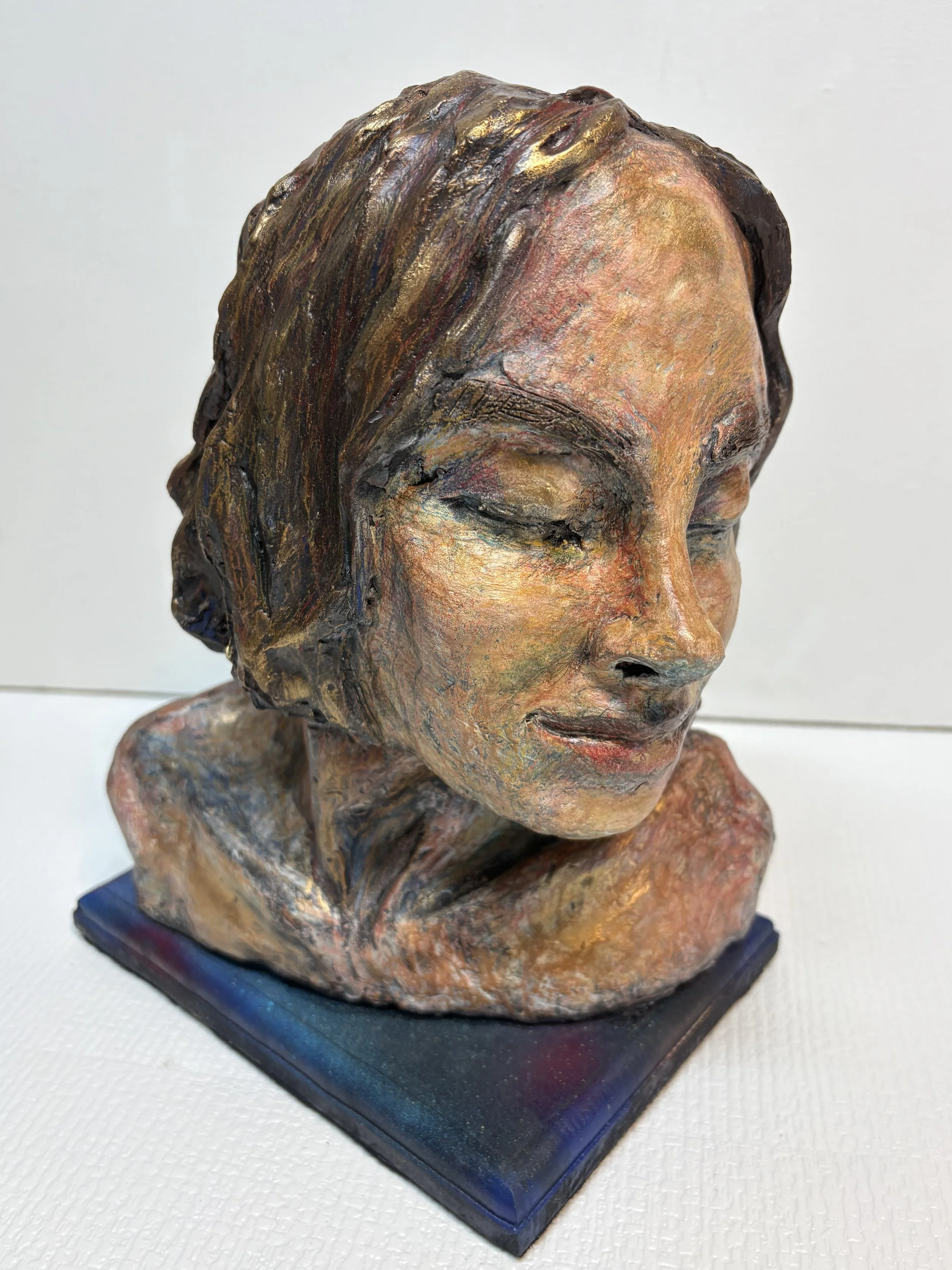 A colorful sculpture of a woman's head with eyes closed, featuring textured, layered paint and a short hairstyle, mounted on a square base.