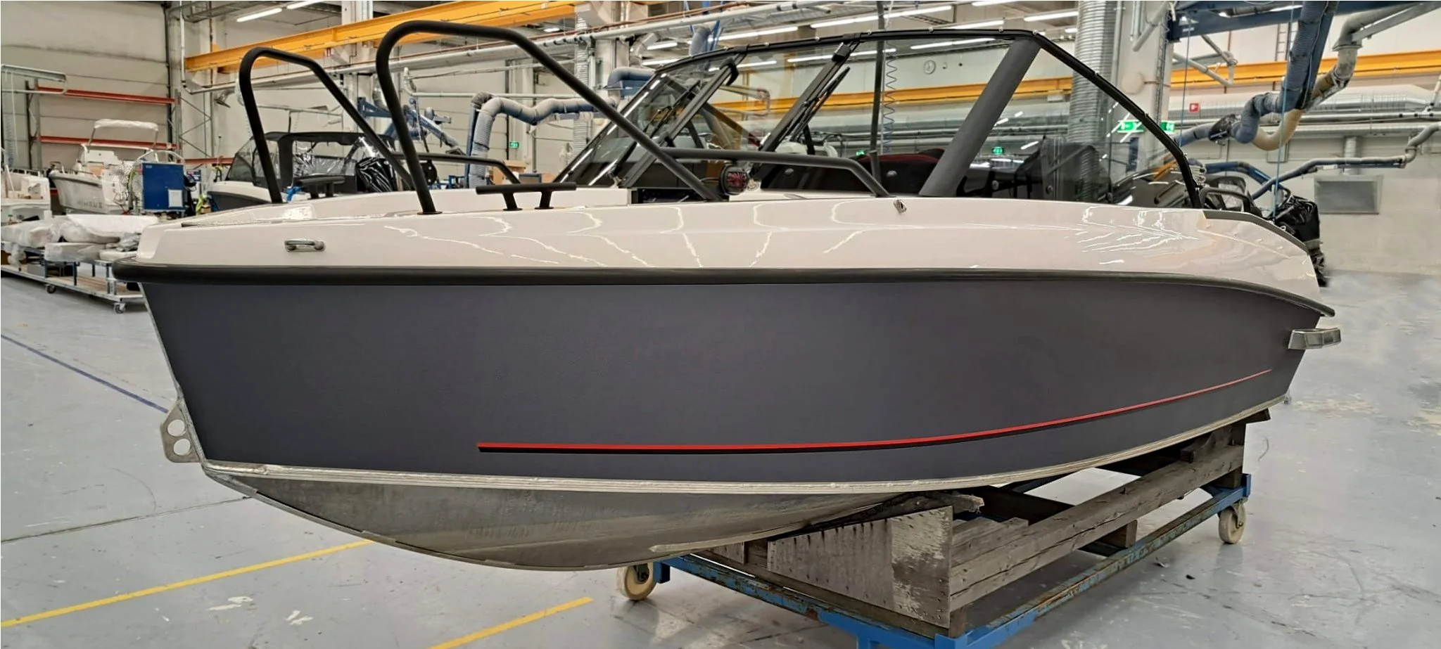 Huollettu vene sisätiloissa tehtaassa tai varastossa, valko-puna-, harmaa- ja metalliosia näkyvissä.