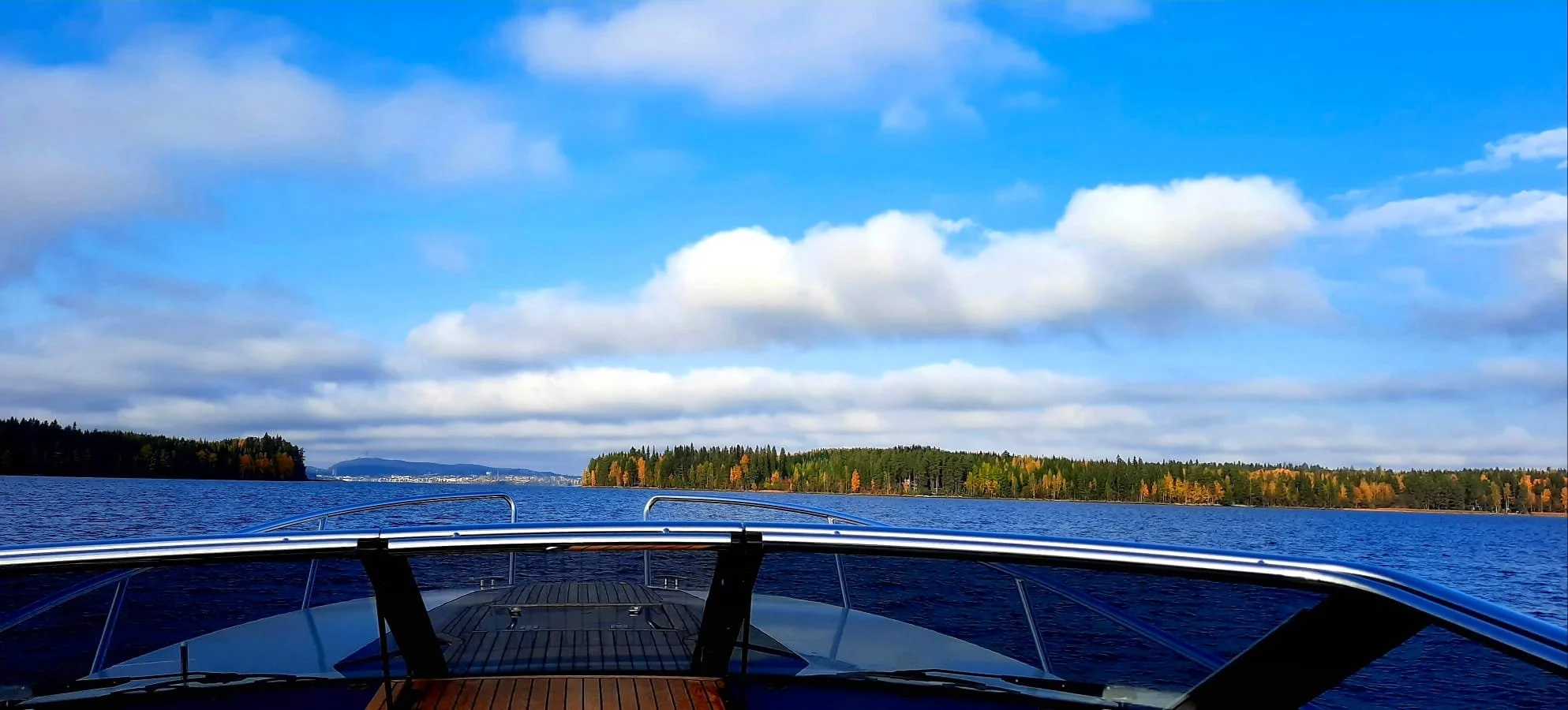 Näyttävä maisemakuva vesiliikenteen veneestä järven yllä, saaristo ja pilvinen taivas näkyvät taustalla.