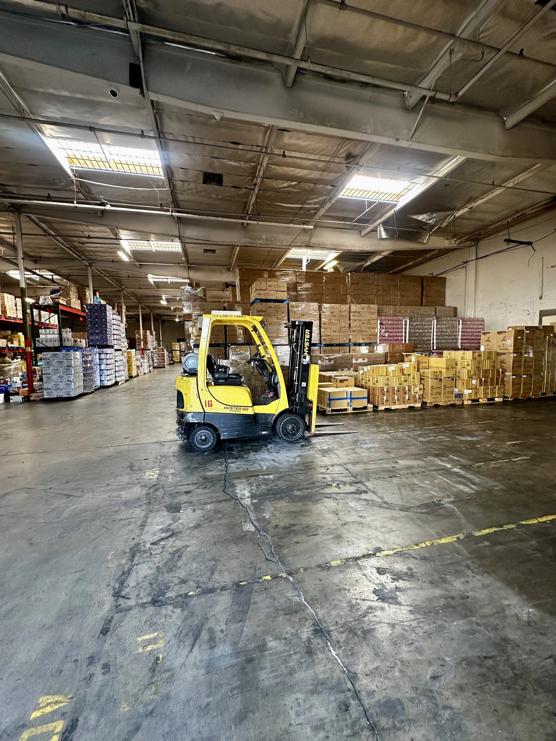 A yellow forklift inside a warehouse with stacks of boxes and pallets.