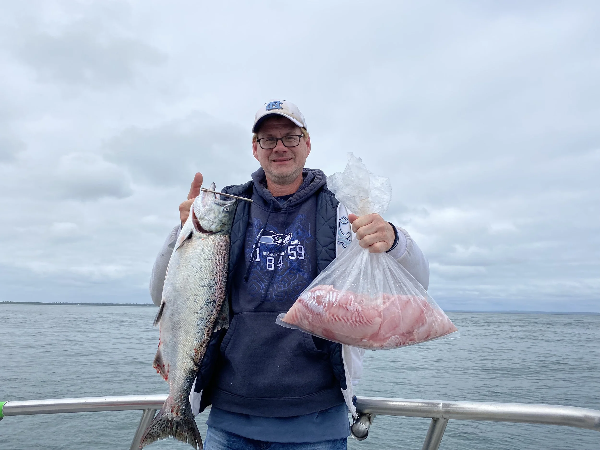 Man smiling and holding a salmon with a bag of fillet rockfish from a combo fishing charter on the tequila too, in Westport, wa
