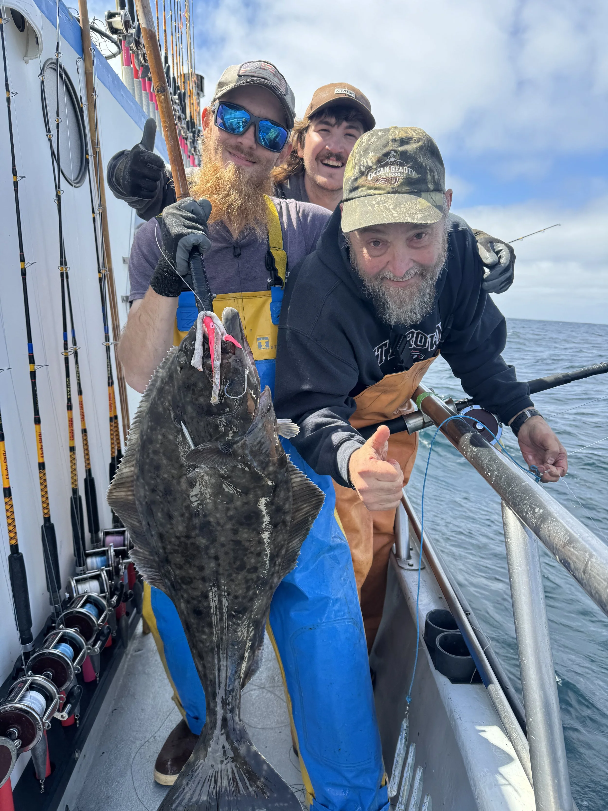 Our deckhands smiling and giving an inviting thumbs up holding a halibut on charter fishing trip in Westport washington