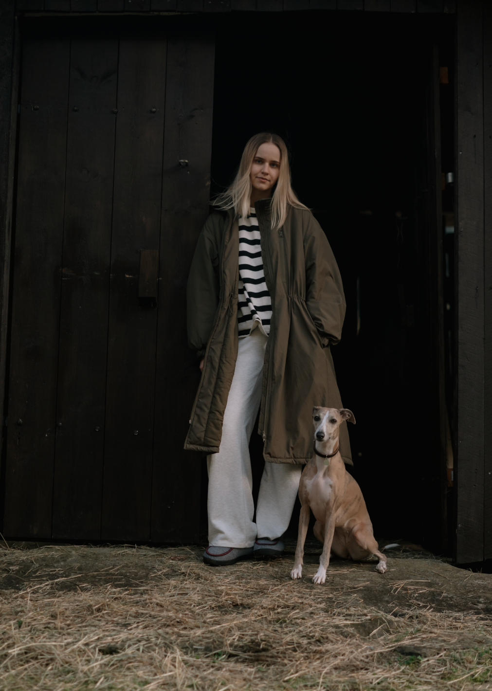 En ung kvinne står foran en mørk dreng med en hund som sitter ved føttene hennes.