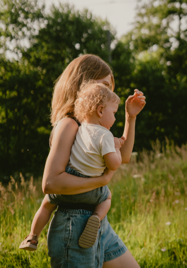 En kvinne bærer en liten gutt på armen mens de går i en grønn utendørs setting