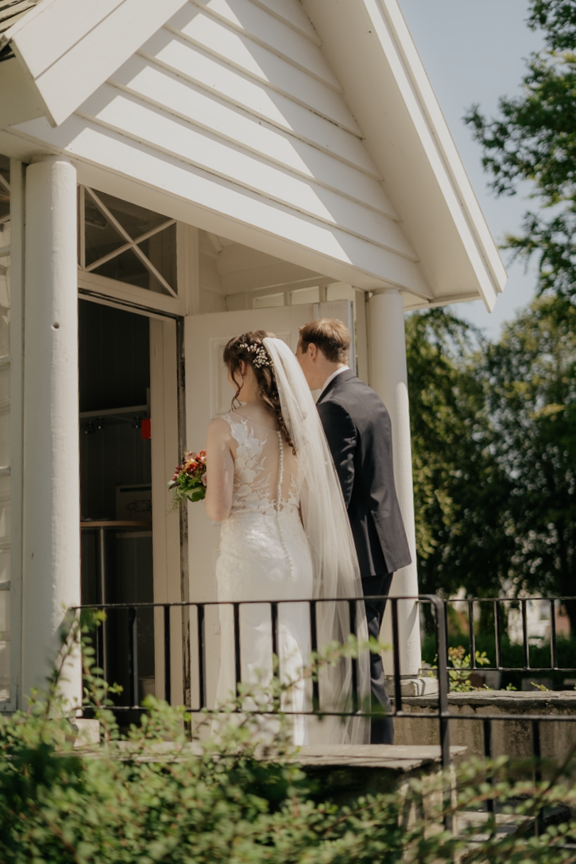 Bryllupspar som står utenfor en hvit liten bygning