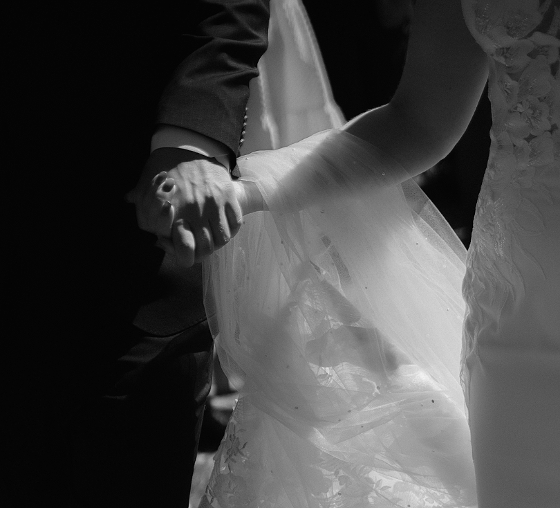 To personer holder hverandre i hånden under et bryllup, en av dem er iført brudekjole, og den andre trolig en dress.