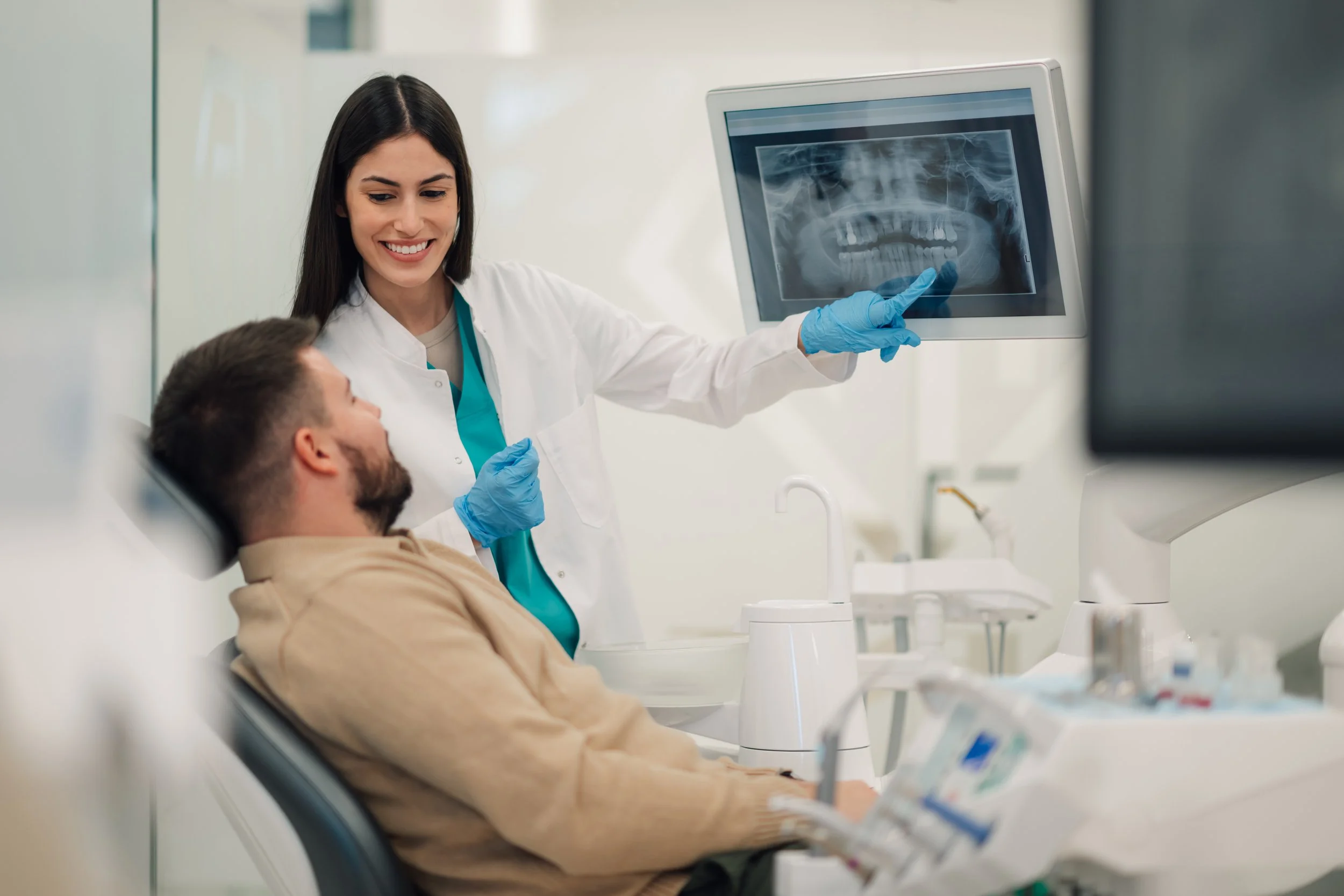 Dentist shows an X-ray of a patient's teeth on a computer screen in a clinical setting.