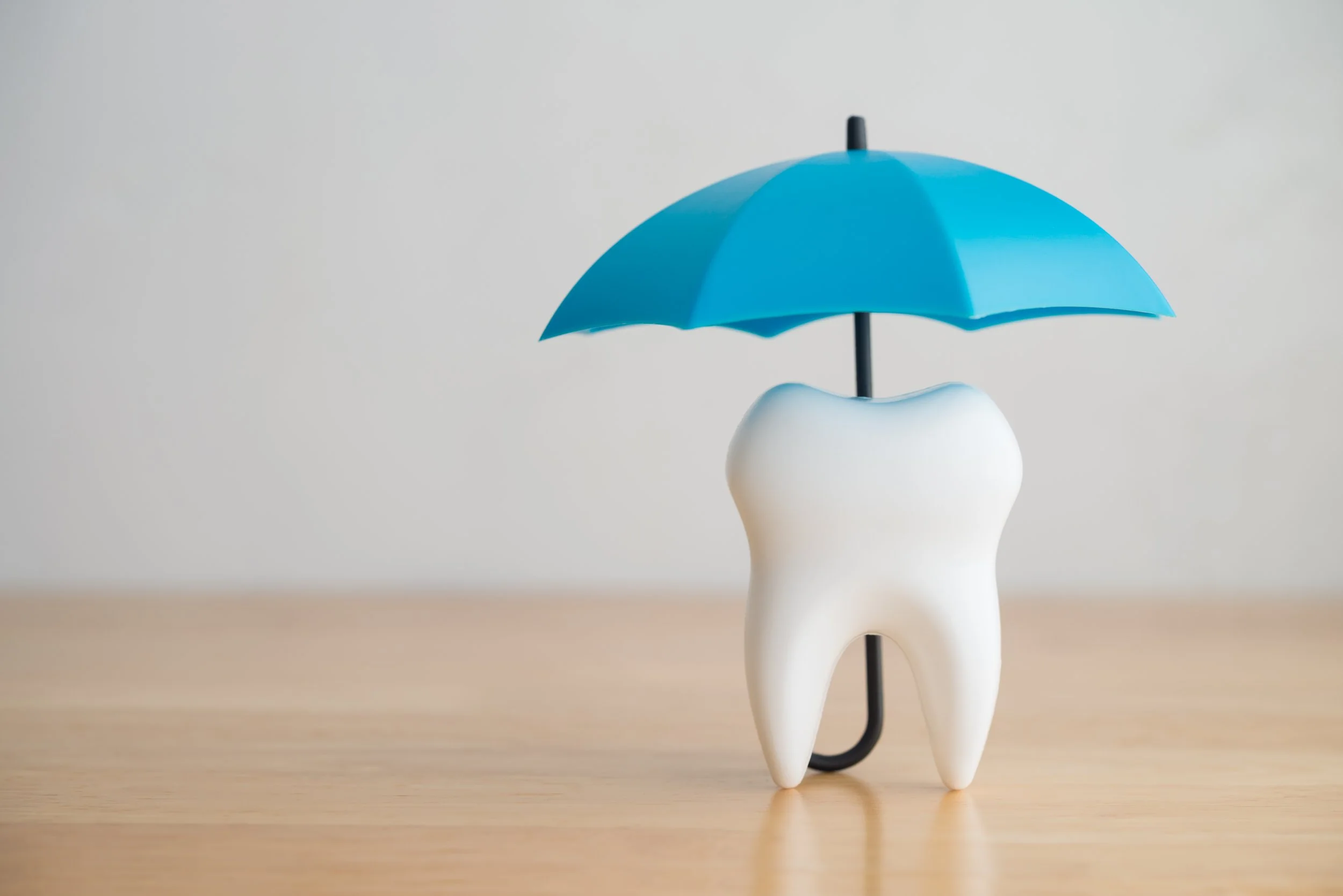 A model tooth holding a blue umbrella on a wooden surface.