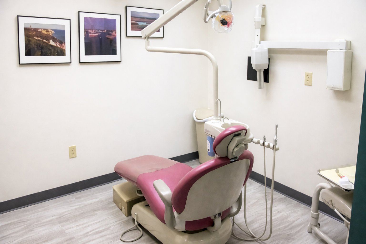 Dental office with dental chair, overhead light, and medical equipment, decorated with framed landscape photographs on the wall.