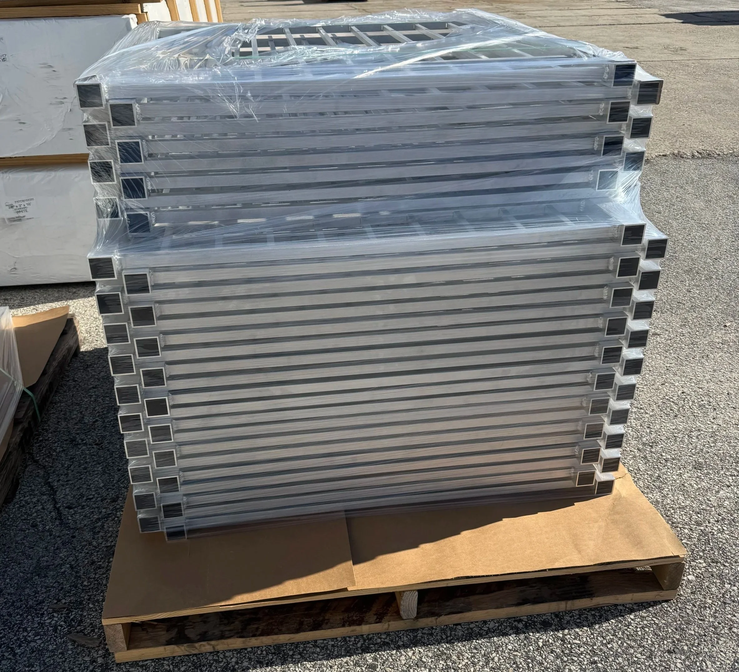 Stack of aluminum L-shaped metal profiles wrapped in plastic on a wooden pallet outdoors.