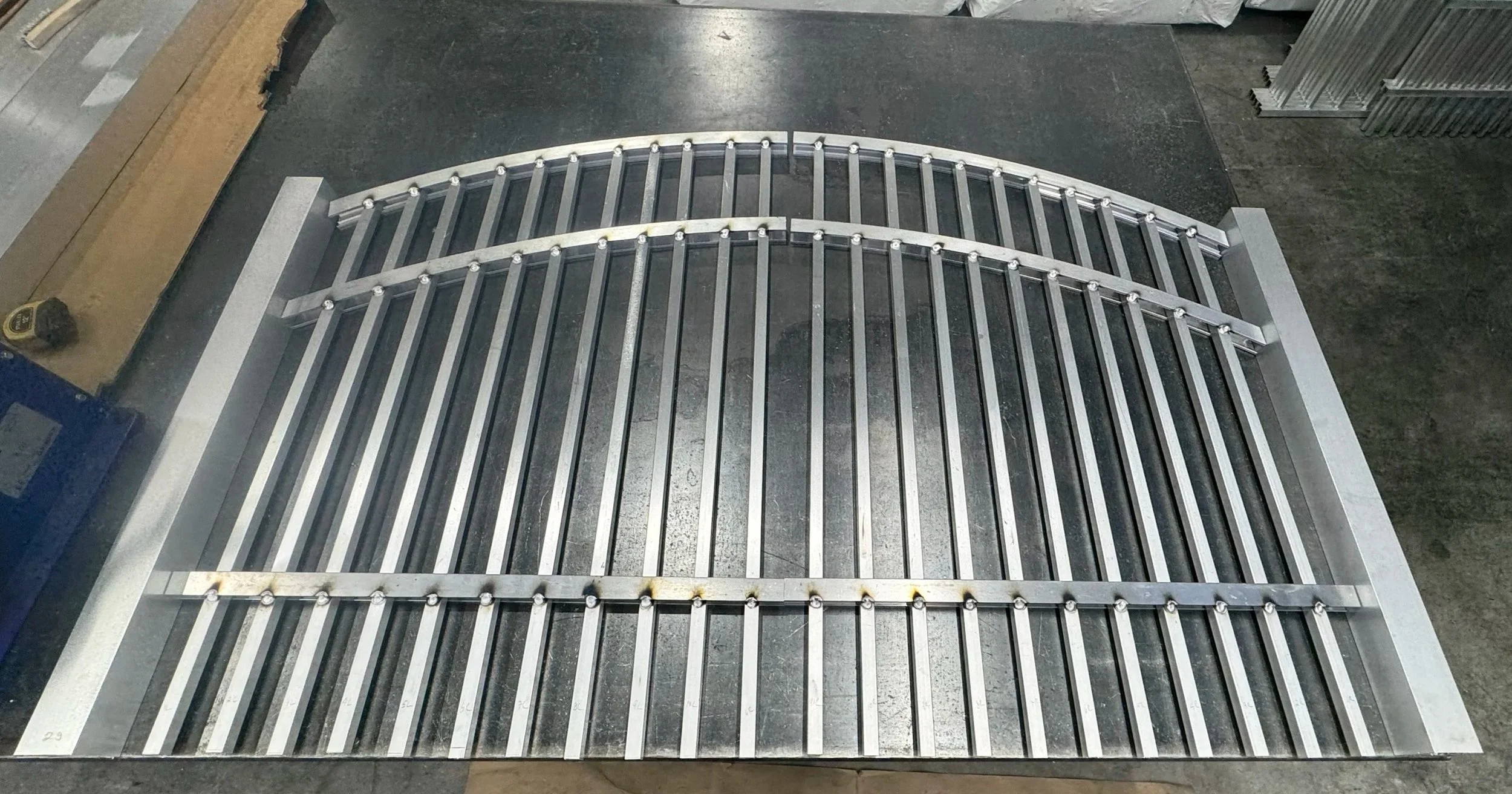 Aluminum gate frame with curved top bars and vertical bars, placed on a workbench in a workshop.